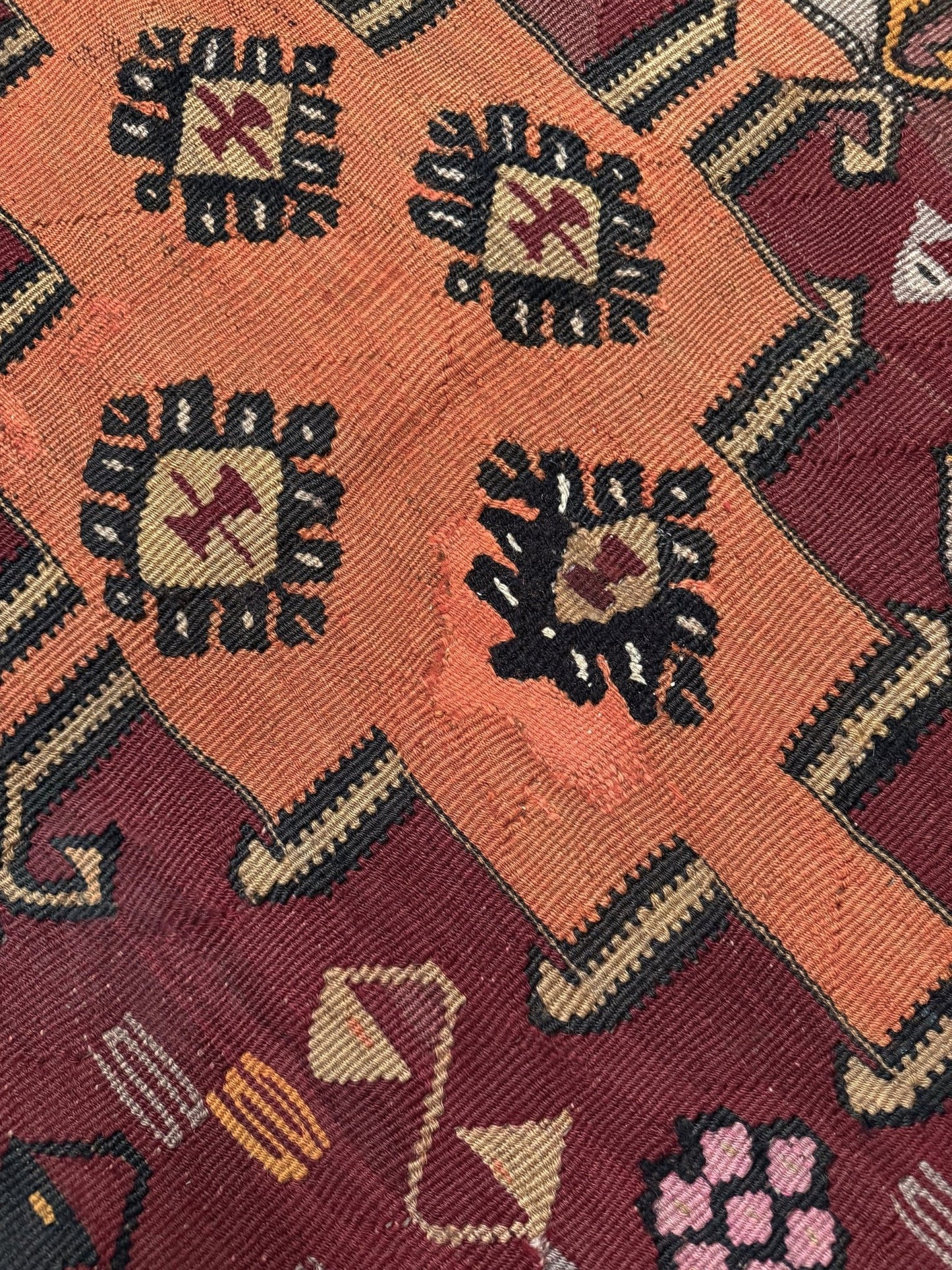 Close-up of a patterned fabric with geometric designs on a red background. Vintage Kurdish Kars kilim, featuring maroon red and chestnut brown field, geometric medallions, symbolic tribal motifs and protective symbols, handwoven wool 5x10 flatweave rug