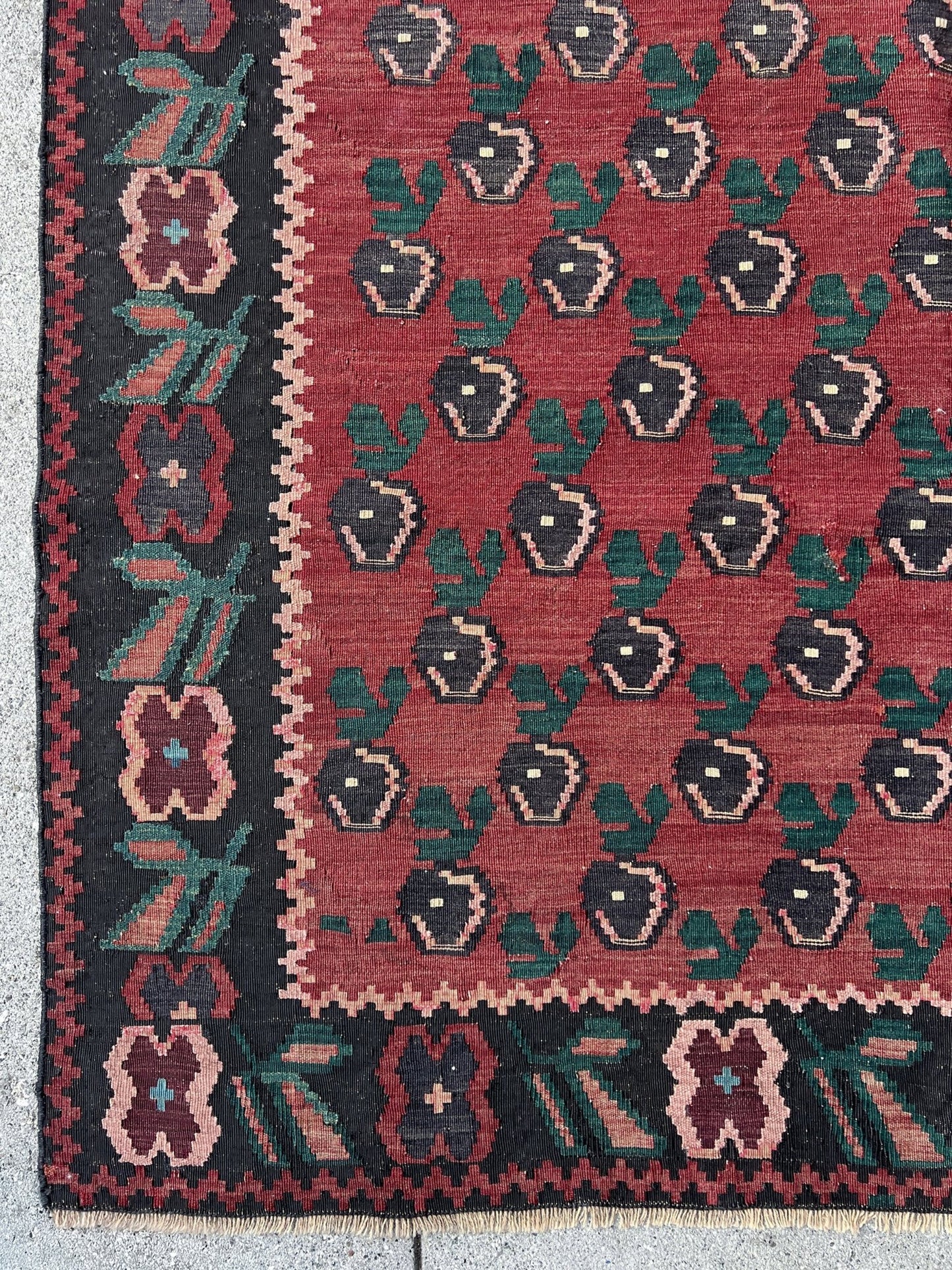 A stunning 1950s vintage Armenian Kilim flatweave rug with a crimson red backdrop, decorated with intricate floral motifs in forest green, blush pink, charcoal black, and creamy yellow accents. This handmade rug, available from the best kilim rug shop in the San Francisco Bay Area, is a versatile piece perfect for a living room, bedroom, nursery, kitchen, or dining area. Its lightweight yet durable craftsmanship makes it both a functional and decorative choice. Free shipping included!