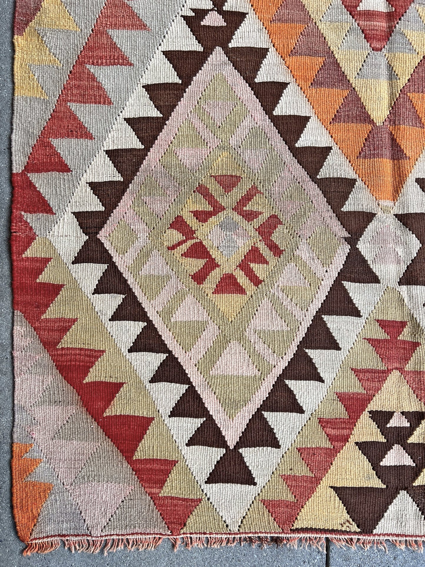 Geometric patterned rug with triangles in various colors on a textured surface. Vintage Mut region Turkish kilim, 4x 7, with large stepped diamond medallions and tribal geometric motifs in faded earthy tones handwoven wool flatweave from the 1960s.