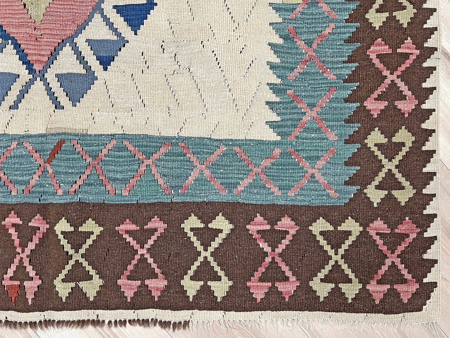 Close-up of a patterned rug with geometric designs in various colors. Vintage Turkish kilim rug, 5x7, with ivory field, pink and blue tribal medallions, and geometric borders in brown and sage tones.