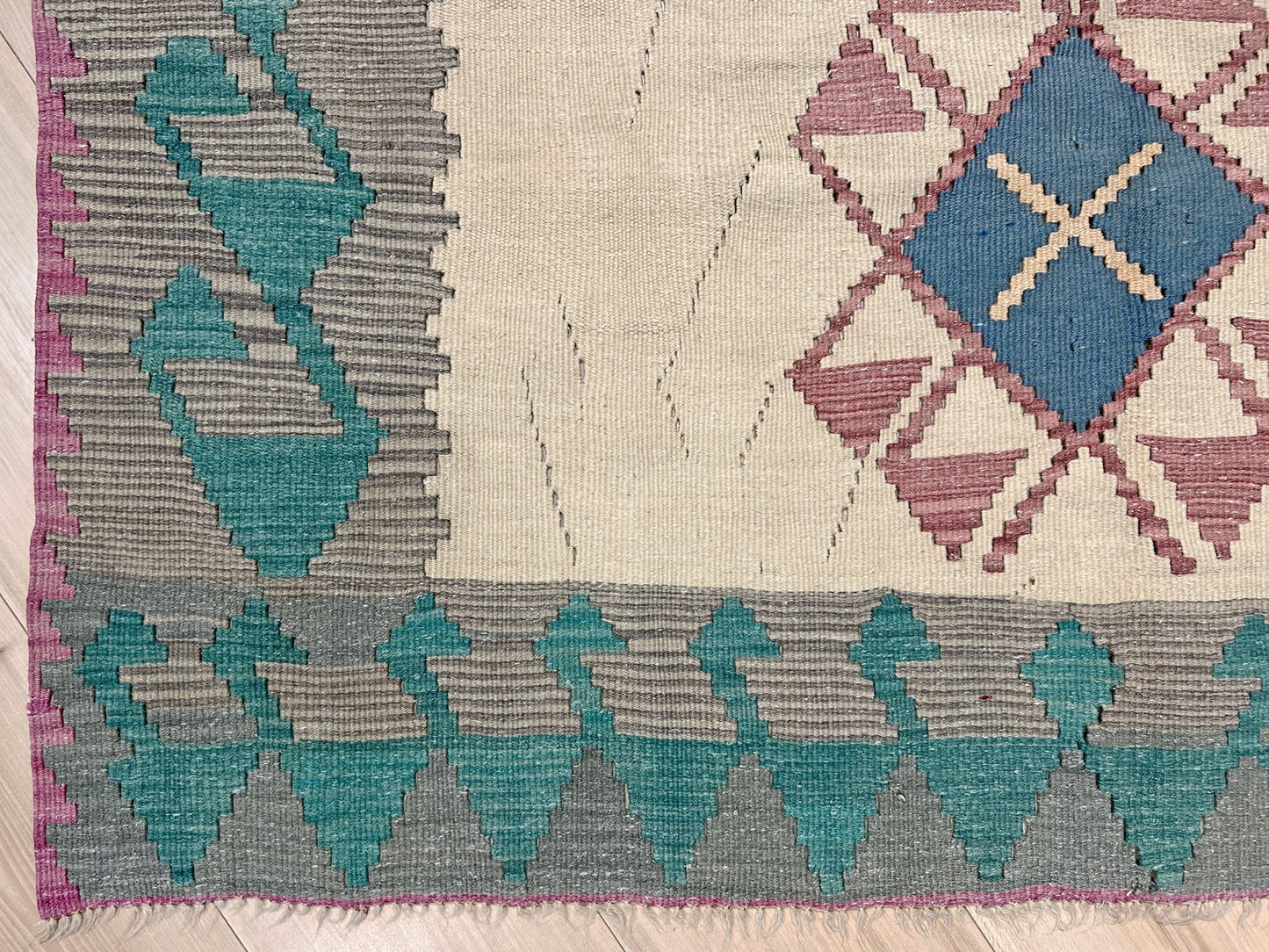 Geometric patterned rug with blue, gray, and purple colors on a wooden floor. Decorative rug with geometric pattern featuring diamonds and cross symbols on a white background. Vintage Turkish kilim rug, 5x7.