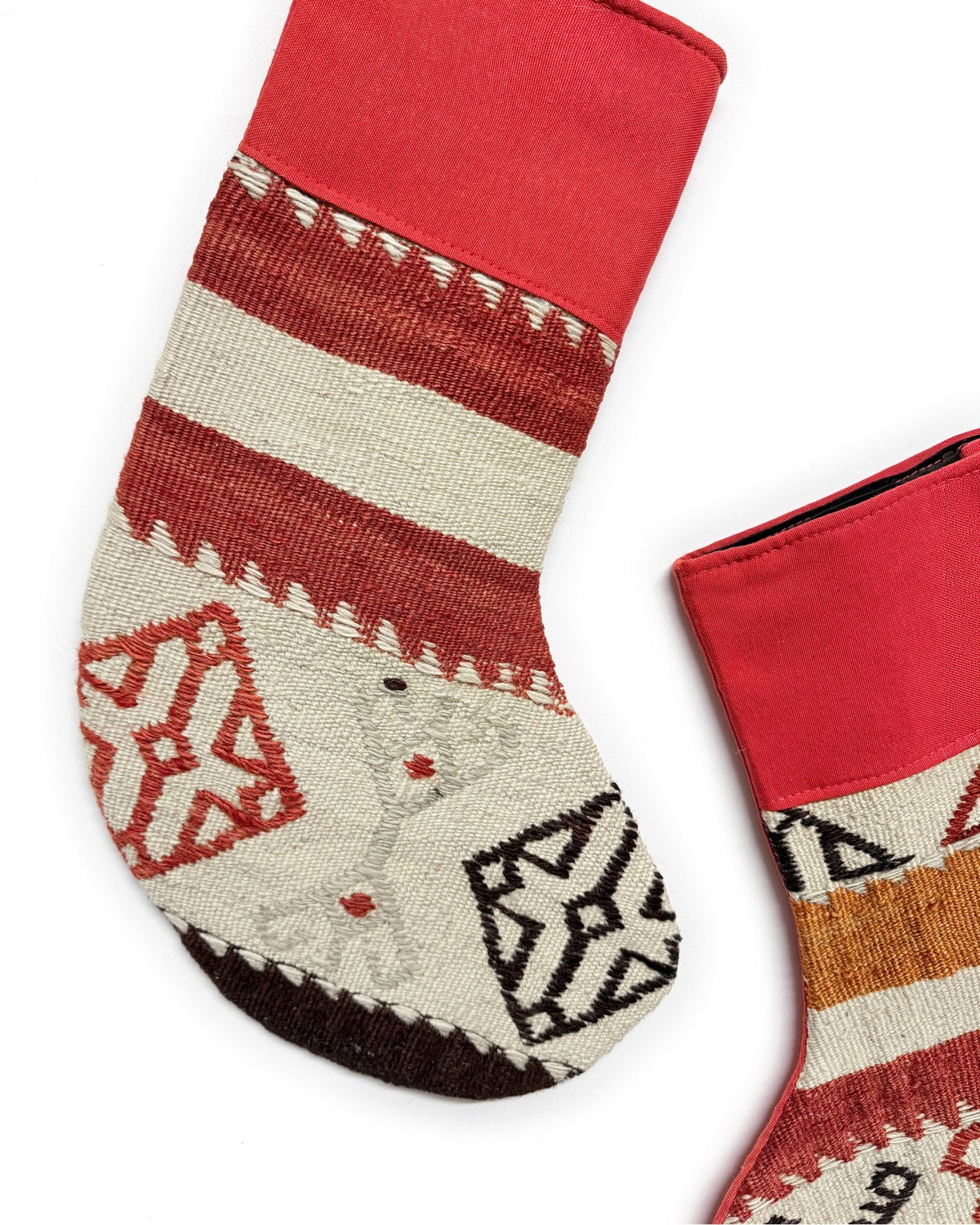 Two Christmas stockings with a Southwestern pattern, featuring red cuffs and hangers, a cream body, and geometric designs in red, brown, and black. Made from vintage wool Turkish rugs.
