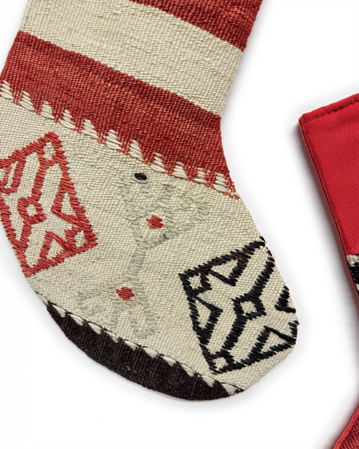 Two Christmas stockings with a Southwestern pattern, featuring red cuffs and hangers, a cream body, and geometric designs in red, brown, and black. Made from vintage wool Turkish rugs.