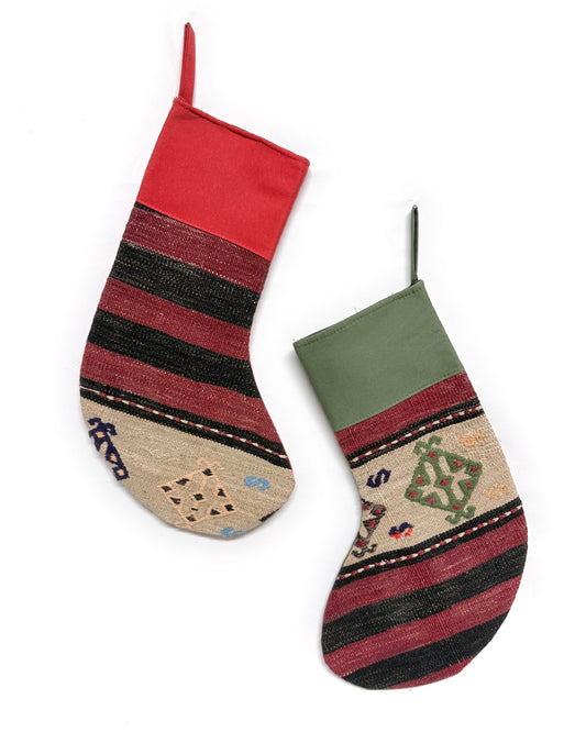 Two Christmas stockings with a Southwestern pattern, featuring red cuffs and hangers, a cream body, and geometric designs in red, brown, and black. Made from vintage wool Turkish rugs.