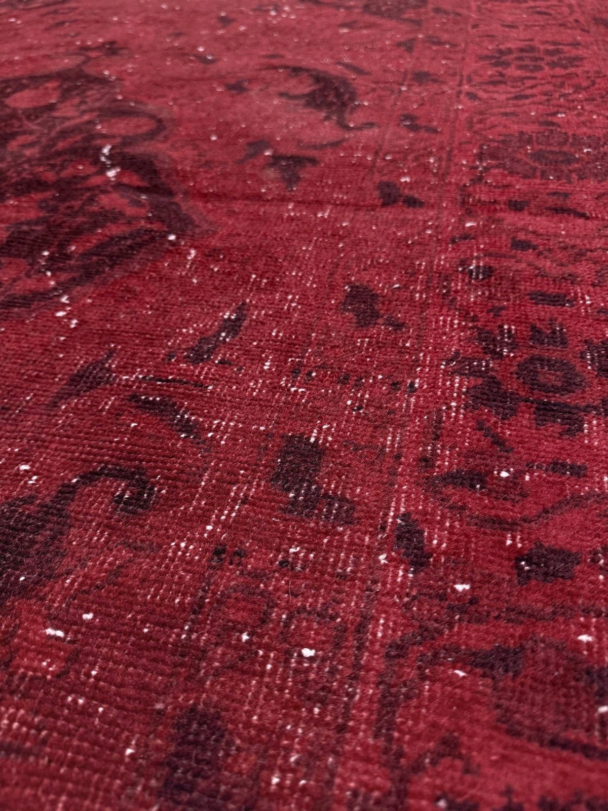 A close-up of a red patterned rug with a distressed, vintage-style design and subtle sheen. Moody red overdyed Turkish rug with distressed vintage pattern, deep burgundy red field, tonal medallion and border design, handmade wool accent rug 5x7 from Indigo Rugs Burlingame Bay Area