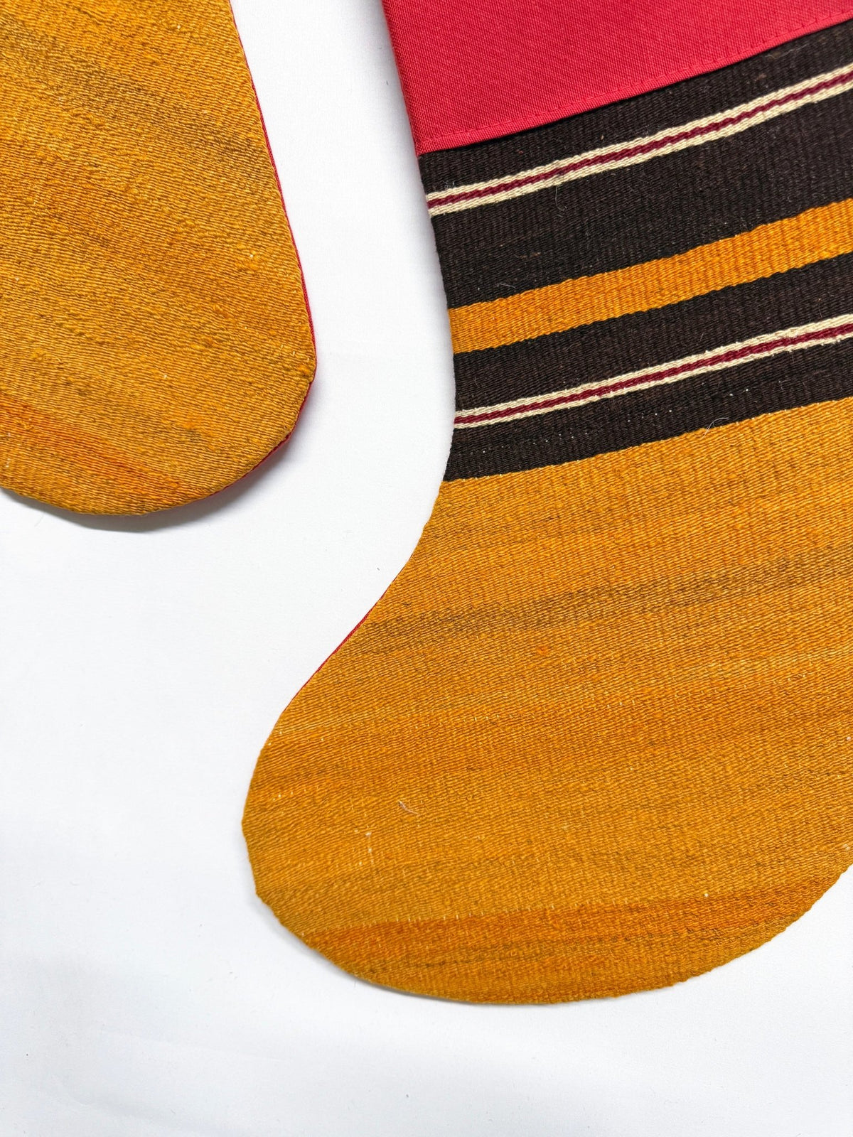 Two Christmas stockings with a striped pattern in red, black, and yellow, shown on a plain white background.