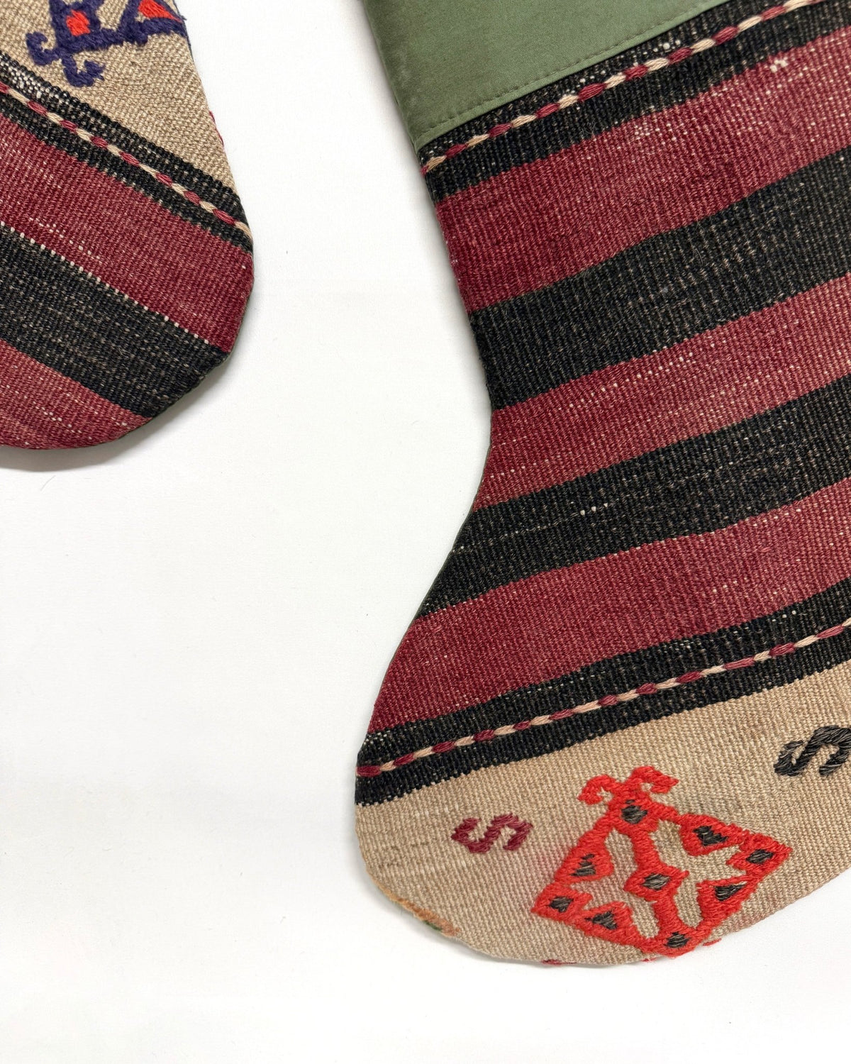 A close-up of a striped knit sock on a white background, showing horizontal bands of beige, burgundy, black, and muted green, with a red playing card graphic and small red lettering near the toe.