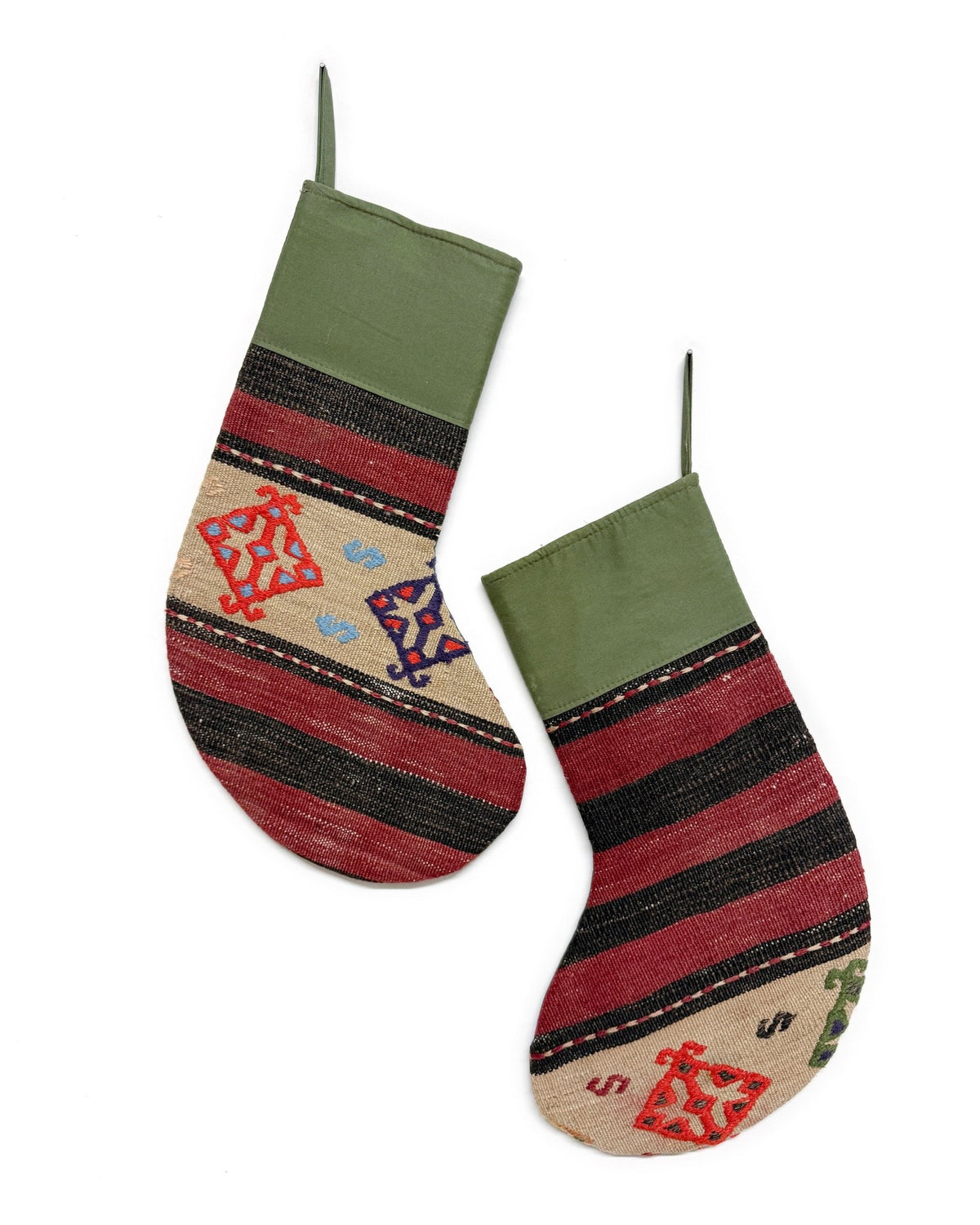 Two handmade Christmas stockings with a rustic kilim pattern, featuring olive green cuffs, red and black stripes, and a beige base with geometric and dollar sign motifs, shown against a plain white background.