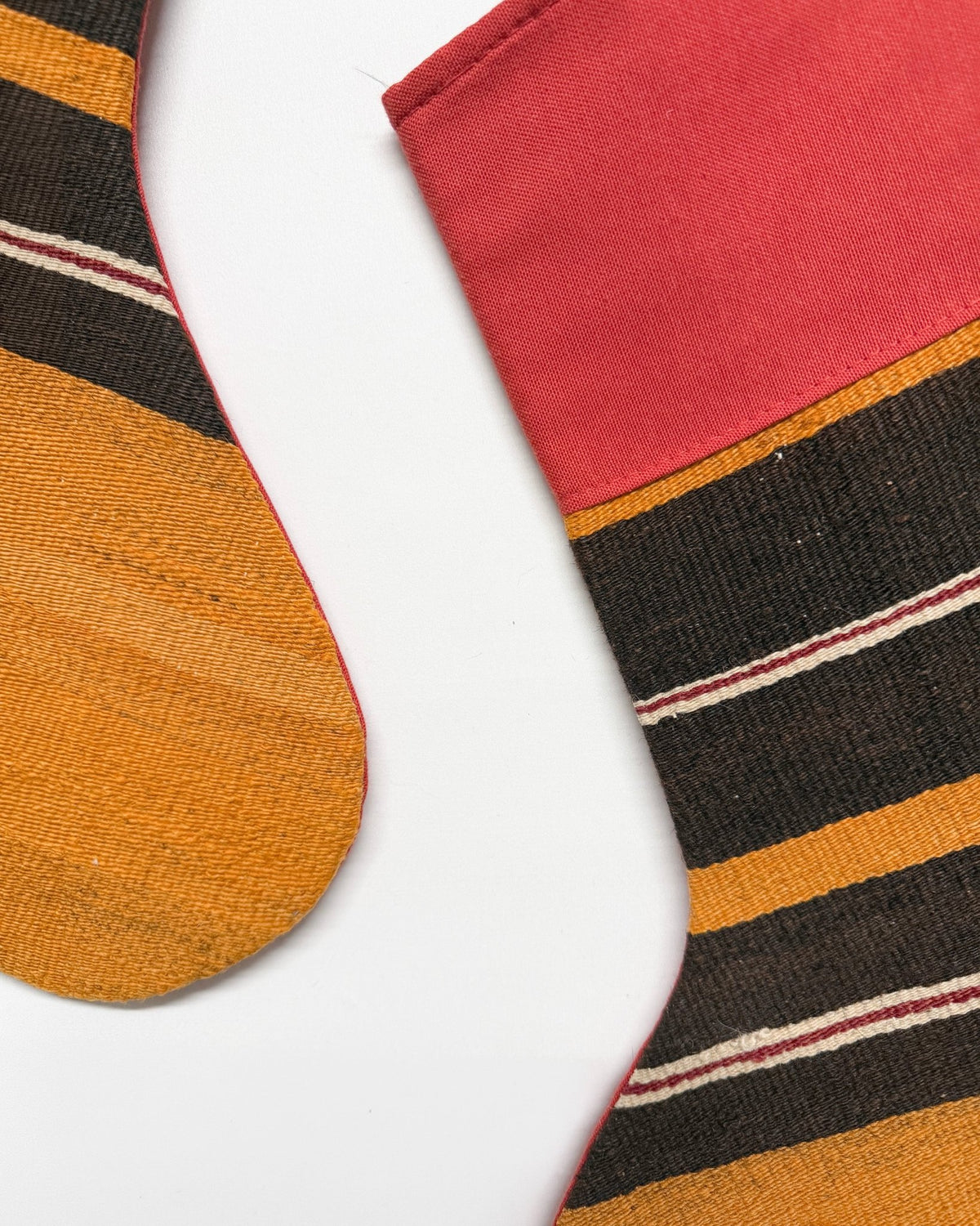Two decorative Kilim Christmas stockings with a woven pattern, featuring a red top, black and tan horizontal stripes, and a golden-yellow textured bottom, shown against a plain white background.