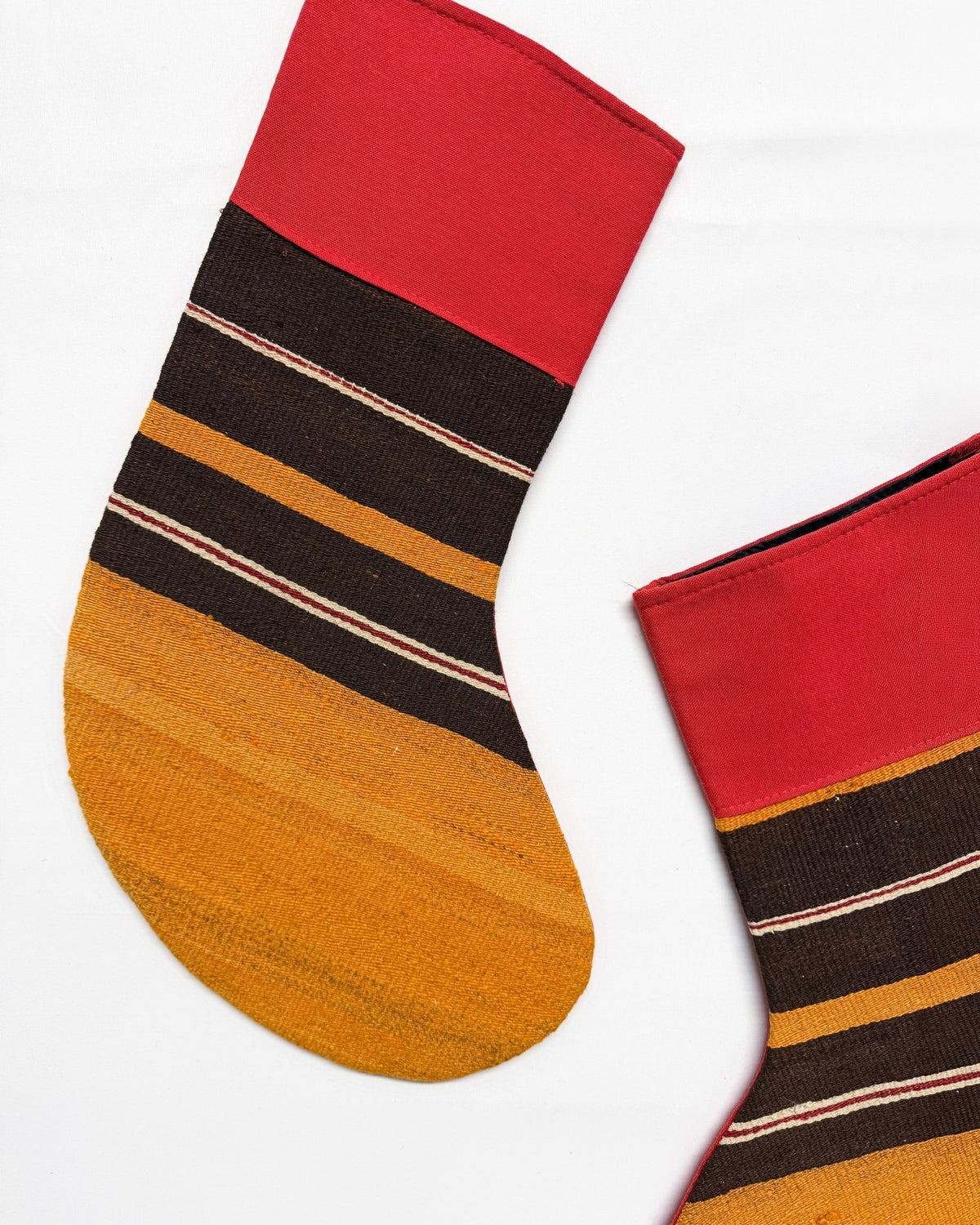 Two decorative Kilim Christmas stockings with a woven pattern, featuring a red top, black and tan horizontal stripes, and a golden-yellow textured bottom, shown against a plain white background.