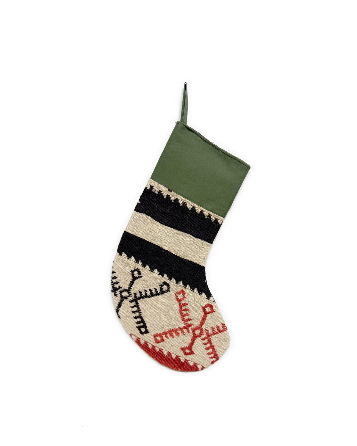 A Christmas stocking handwoven Turkish Kilim with a green cuff, black and cream stripes, and red and black geometric patterns on a cream base, shown against a plain white background.