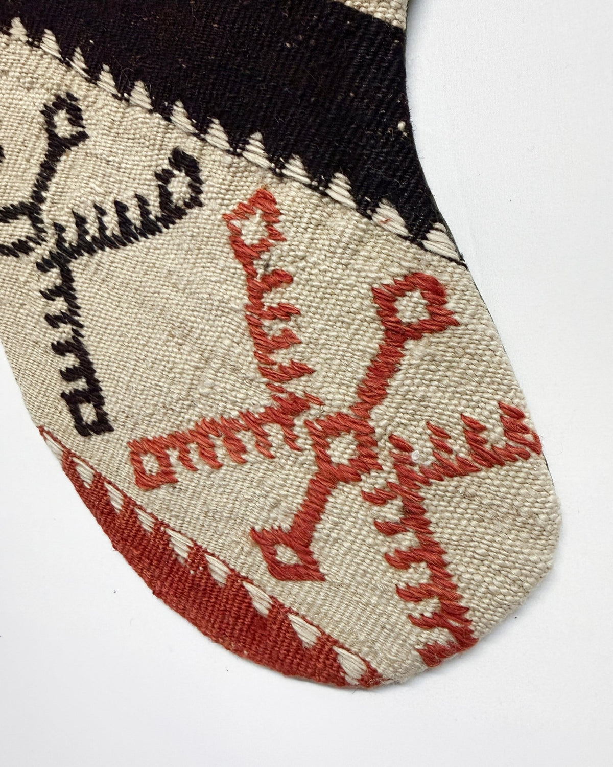 A close-up of a woven textile product, likely a sock or sleeve, featuring a beige base with a black geometric pattern and a red geometric design, set against a plain white background.