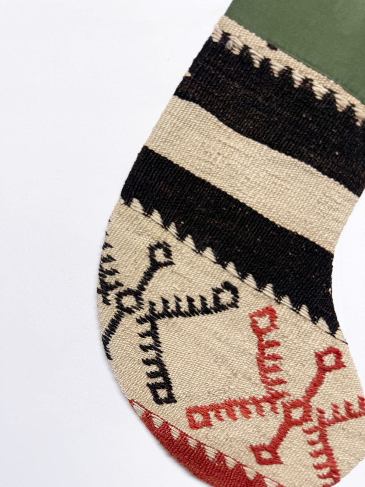 A close-up of a handwoven sock featuring a geometric tribal pattern in black, beige, red, and green.