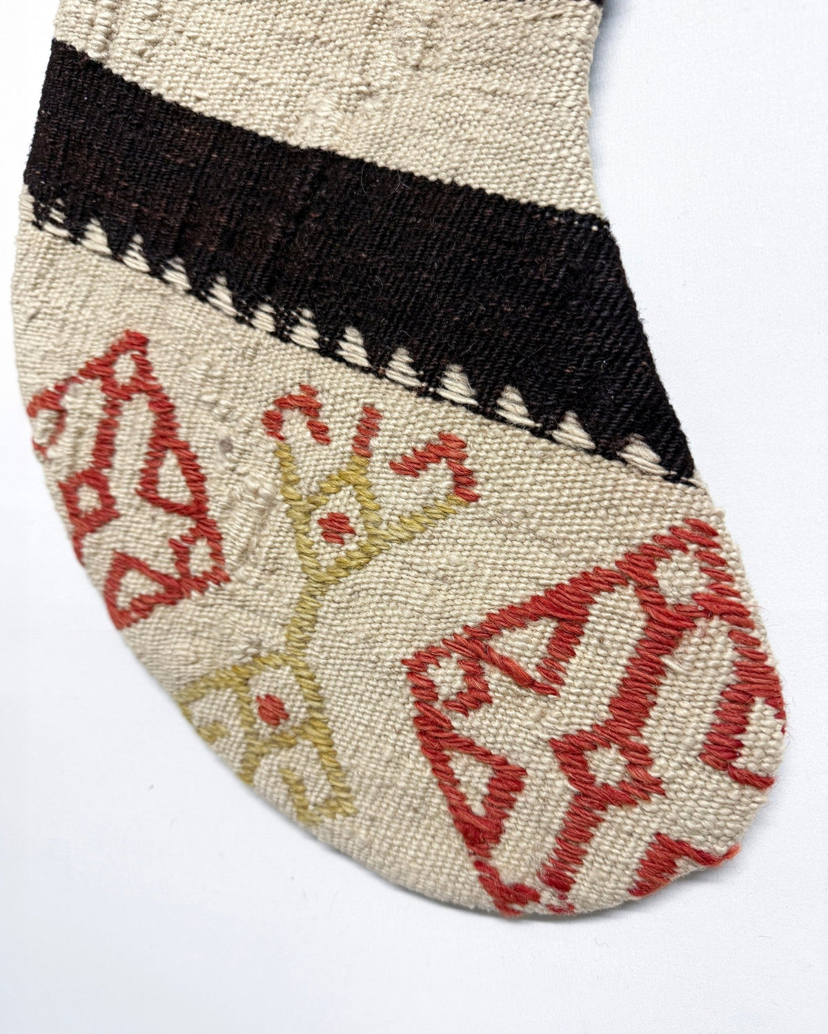 A close-up of a patterned sock on a white background, featuring a beige base with a wide black band, red geometric motifs, and a light yellow motif.