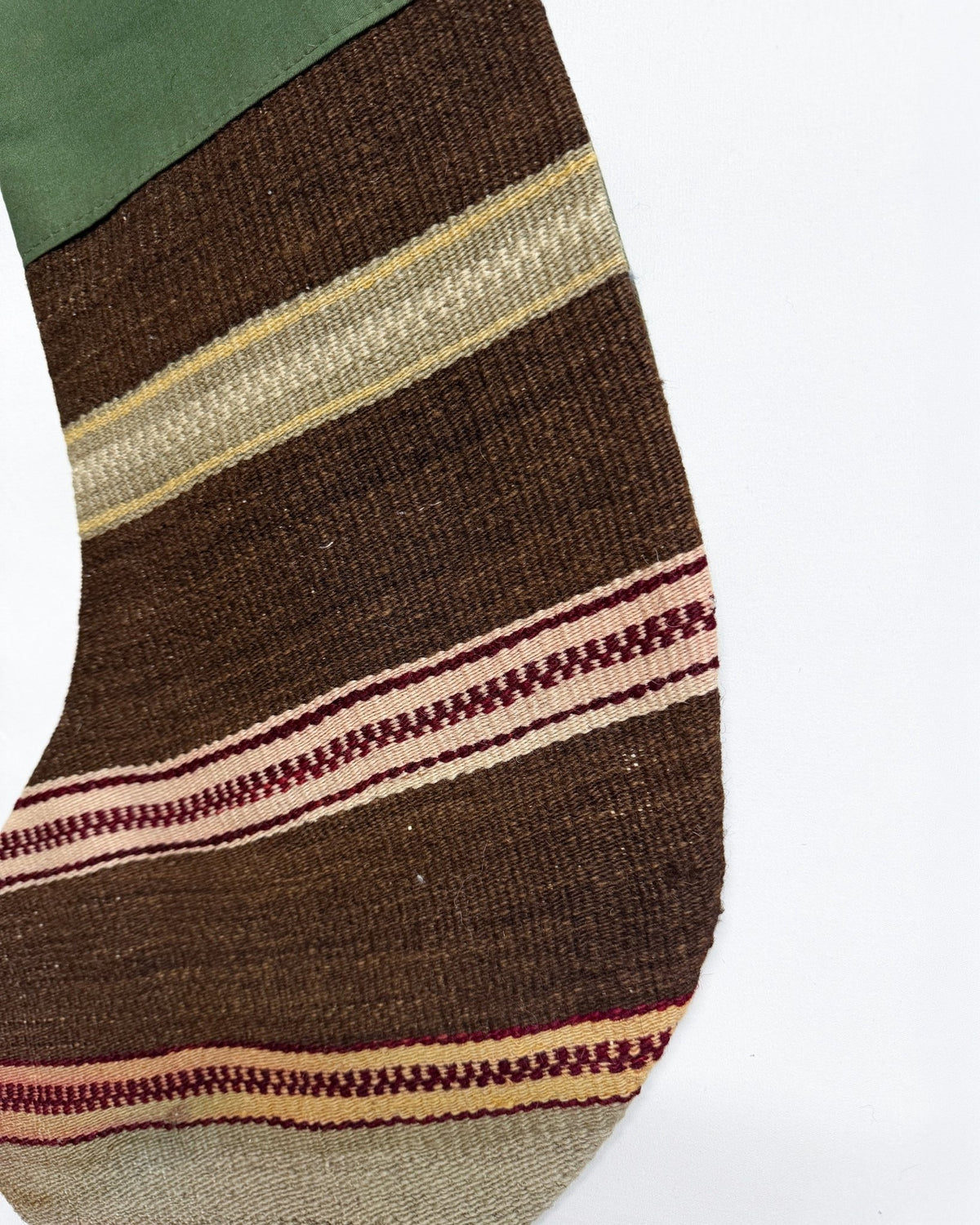 A close-up of a striped knit sock or textile leg warmer in dark brown, beige, cream, burgundy, and muted green, shown against a plain white background.