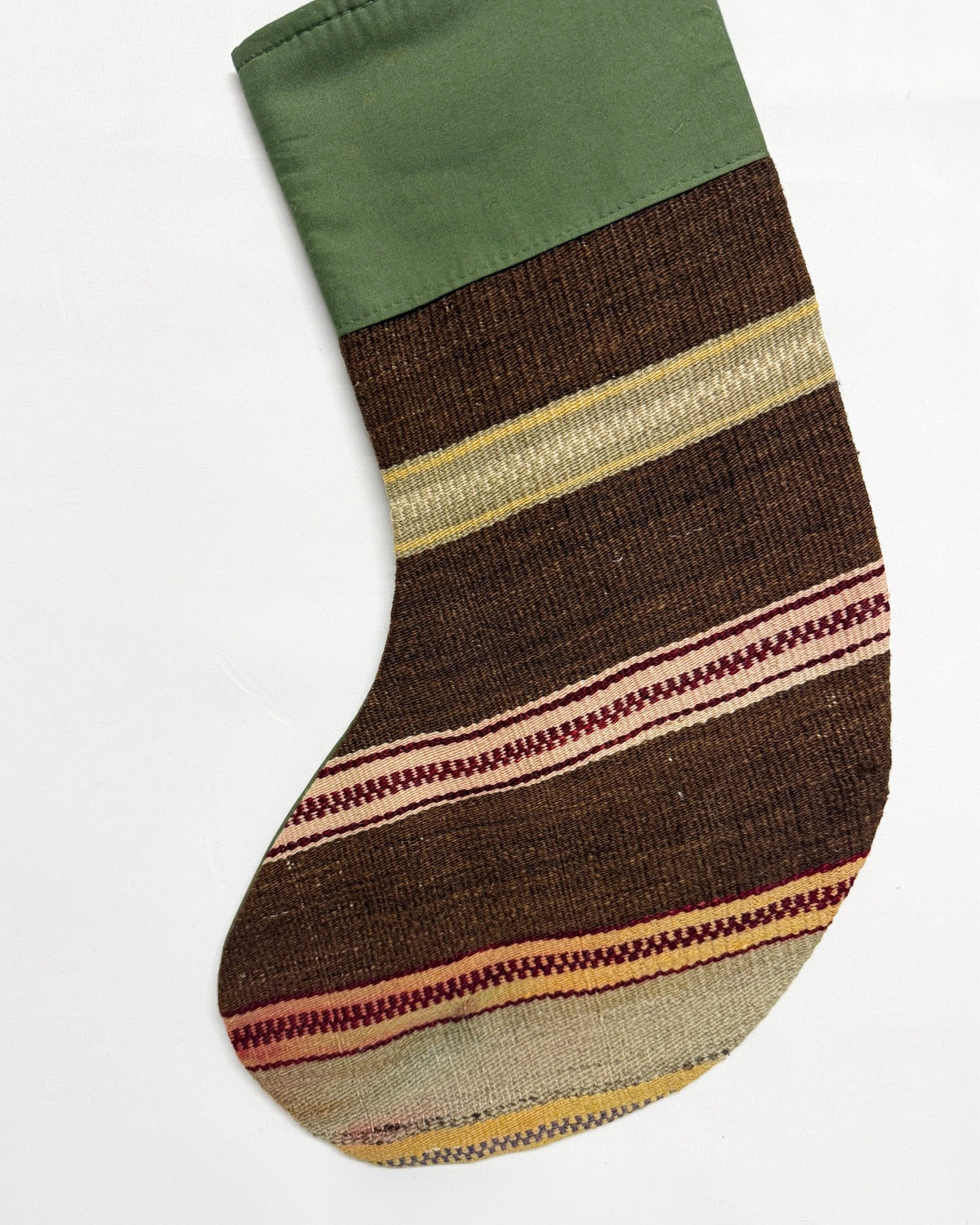 A handwoven Kilim Christmas stocking with a solid olive green cuff and a striped body featuring brown, beige, and red woven patterns, shown against a plain white background.