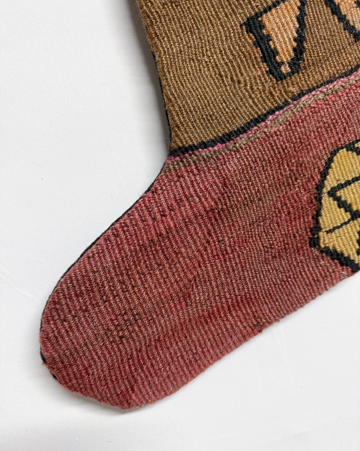 A handmade Kilim Christmas stocking featuring a Southwestern geometric pattern in brown, terracotta, yellow, and black, with a black ribbed cuff and hanging loop.