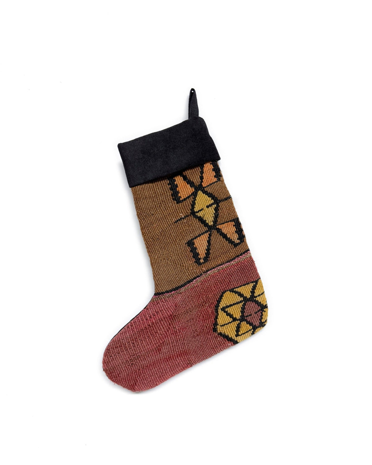 A handmade Kilim Christmas stocking featuring a Southwestern geometric pattern in brown, terracotta, yellow, and black, with a black ribbed cuff and hanging loop.