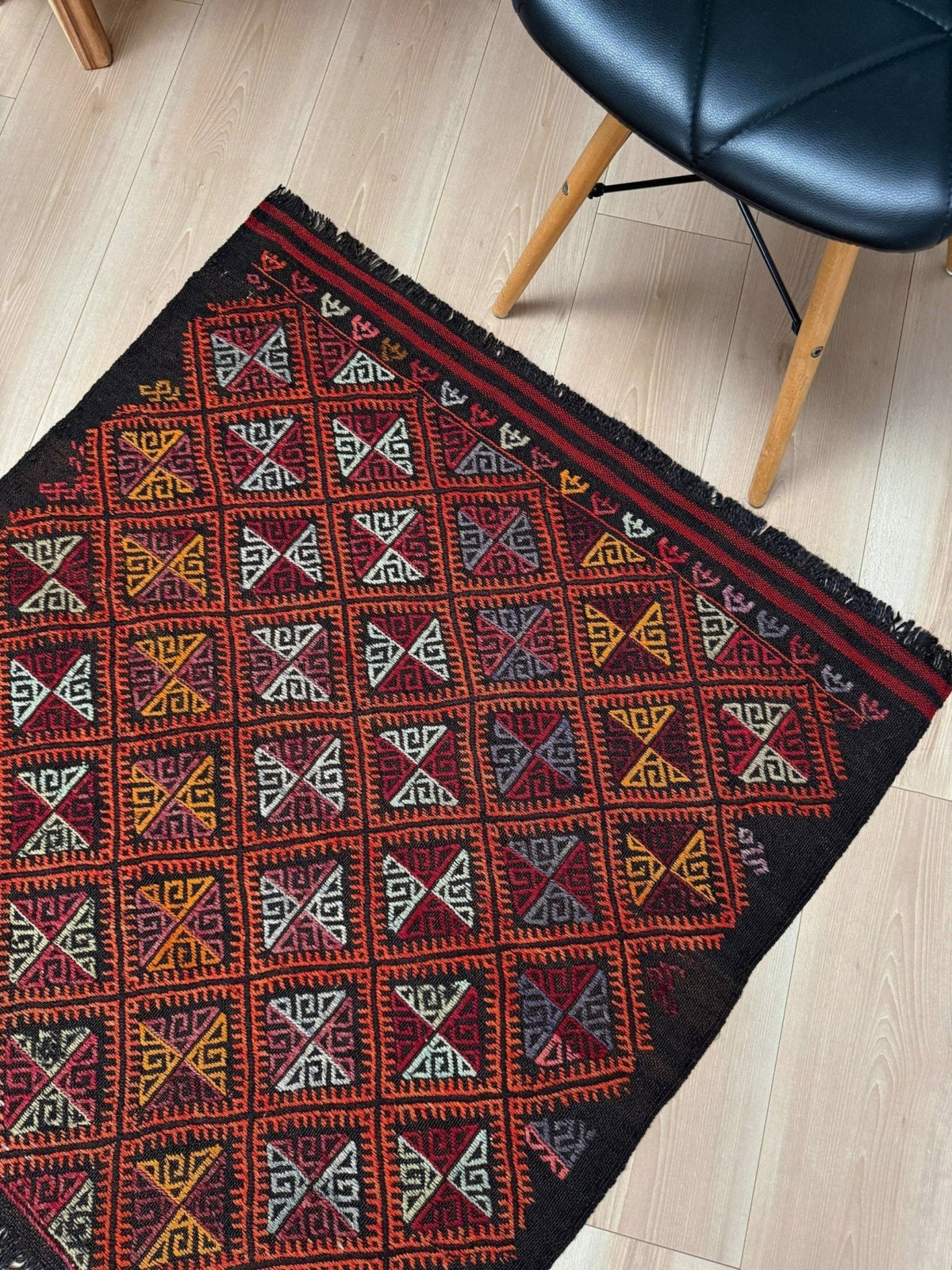 Decorative square turkish kilim rug with geometric pattern on a wooden floor.