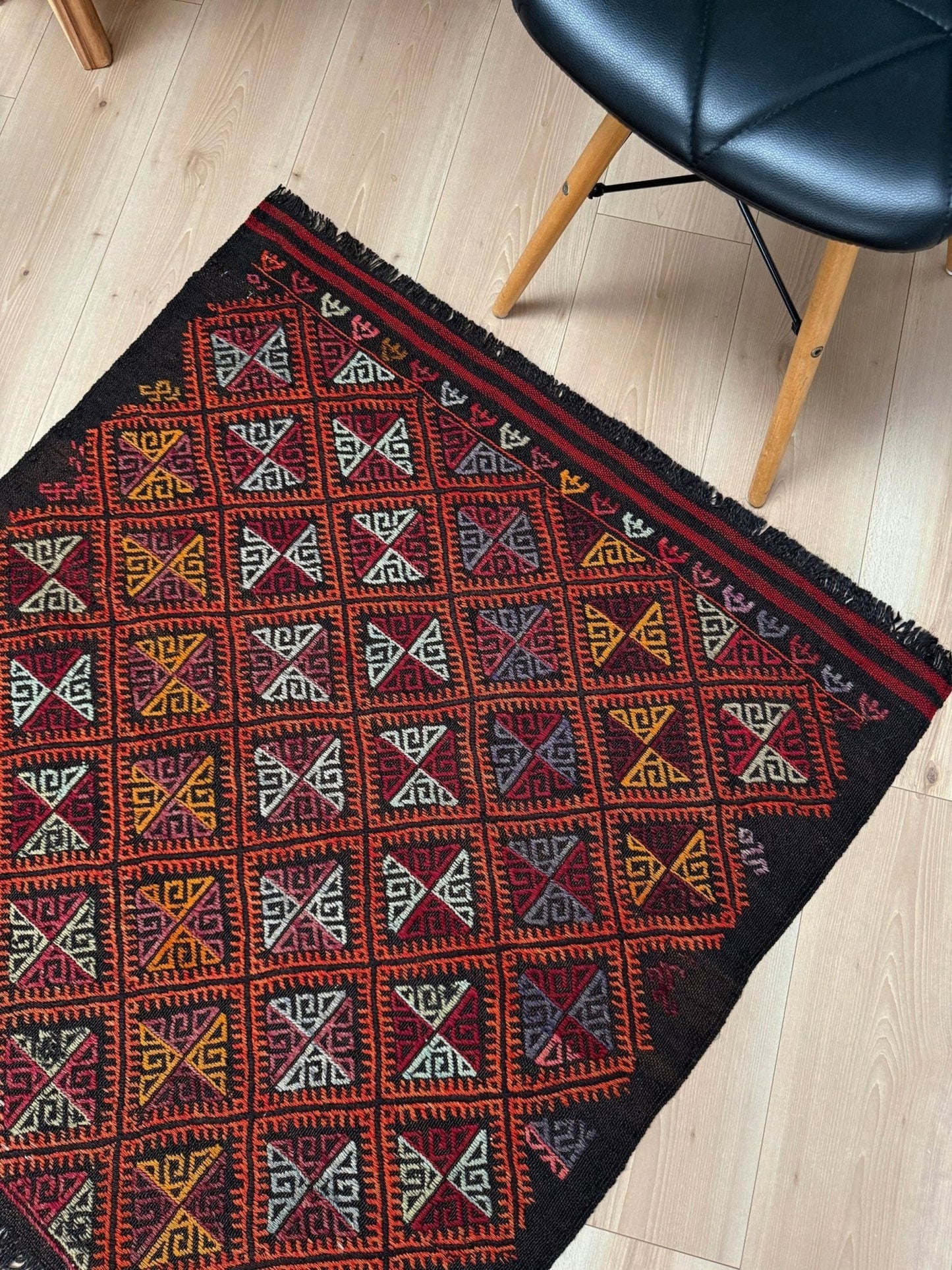 Decorative rug with geometric pattern on a wooden floor, chair visible