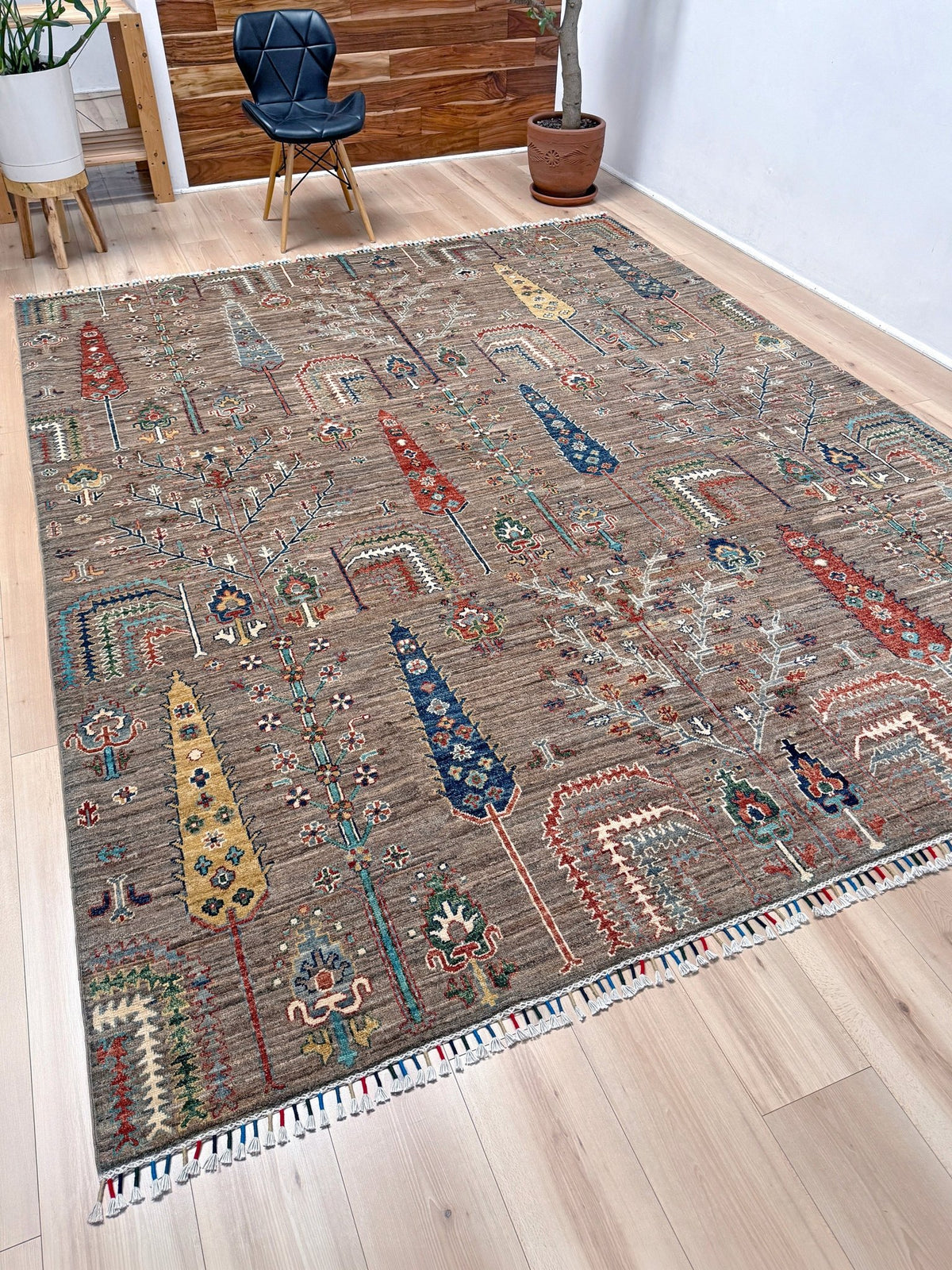 A rectangular area rug with a rustic brown base and colorful geometric tribal patterns, shown on a light wood floor in a modern room setting.