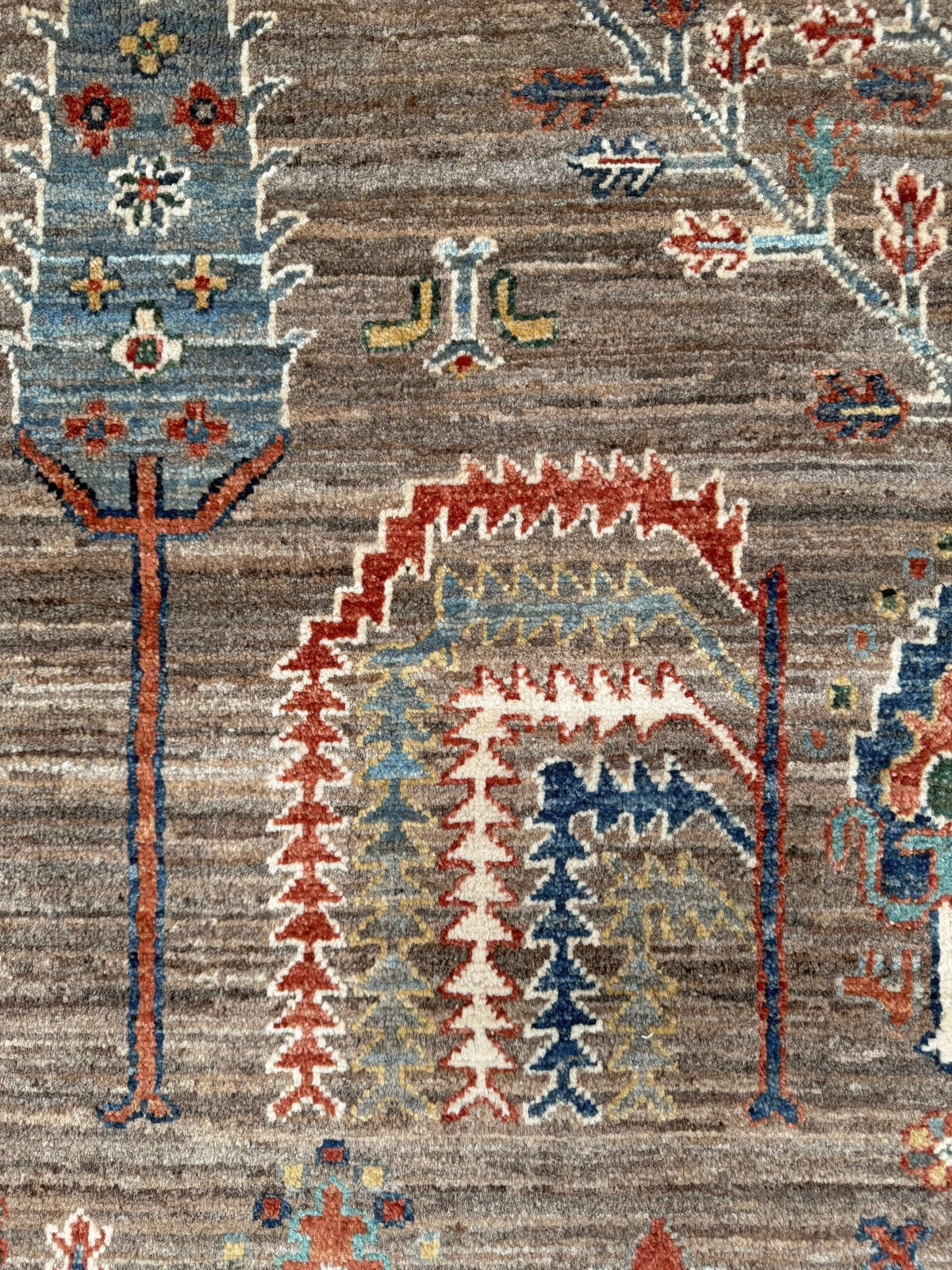 Close-up of a traditional patterned rug with a brown and gray textured base, featuring geometric arch motifs in red, blue, beige, and white.
