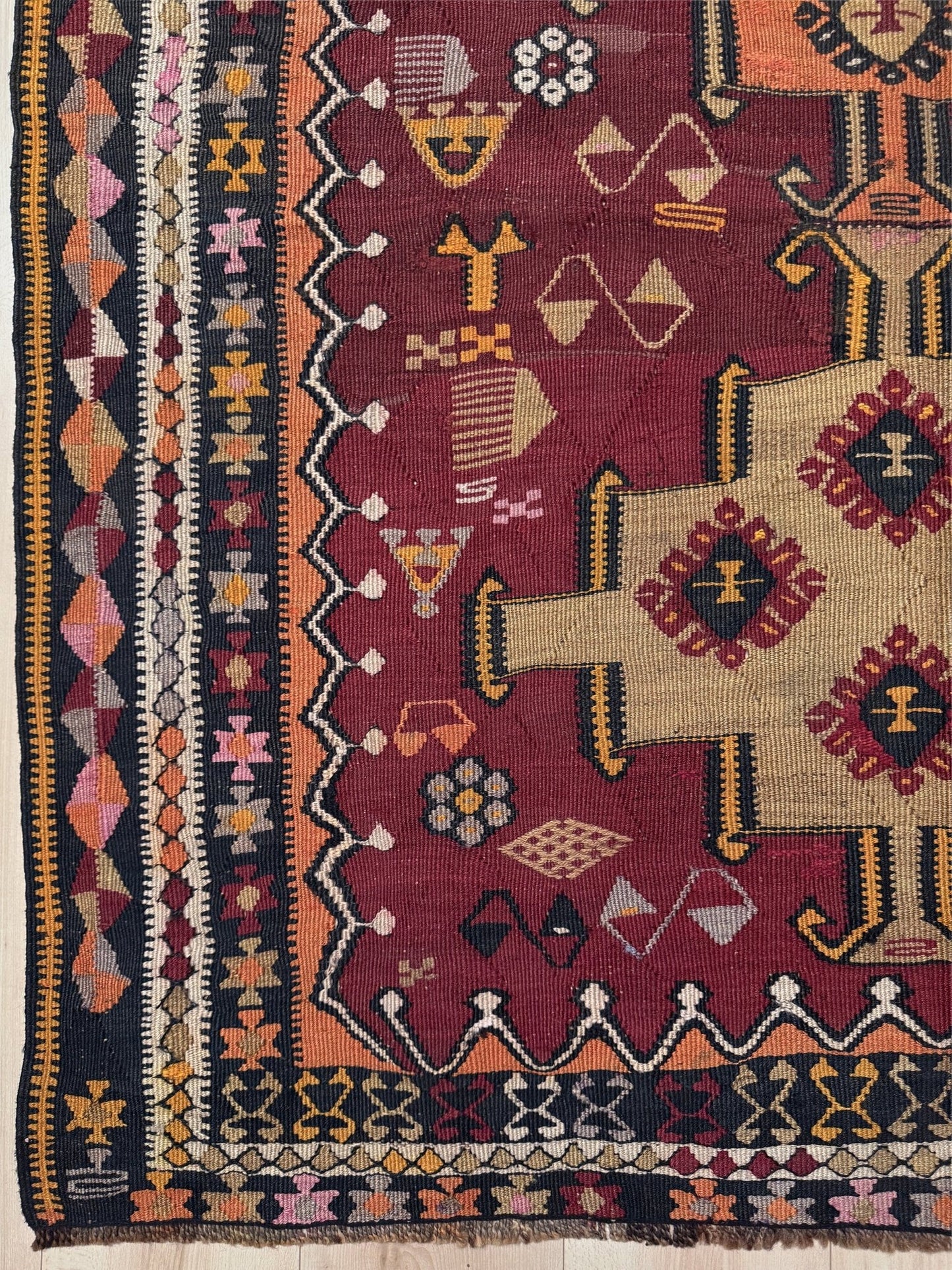 Traditional patterned rug with geometric designs on a wooden floor. Vintage Kurdish Kars kilim, featuring maroon red and chestnut brown field, geometric medallions, symbolic tribal motifs and protective symbols, handwoven wool 5x10 flatweave rug 