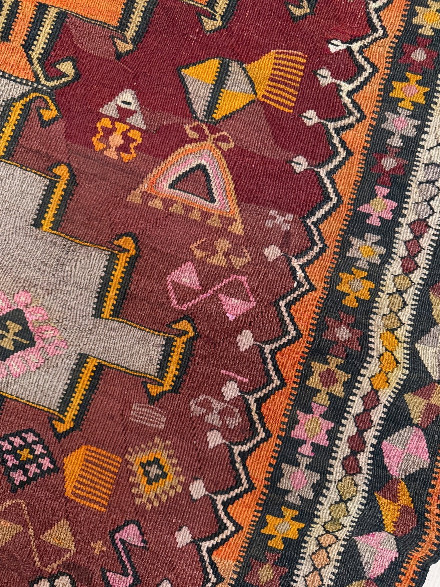 Close-up of a patterned fabric with geometric designs on a red background. Vintage Kurdish Kars kilim, featuring maroon red and chestnut brown field, geometric medallions, symbolic tribal motifs and protective symbols, handwoven wool 5x10 flatweave rug 