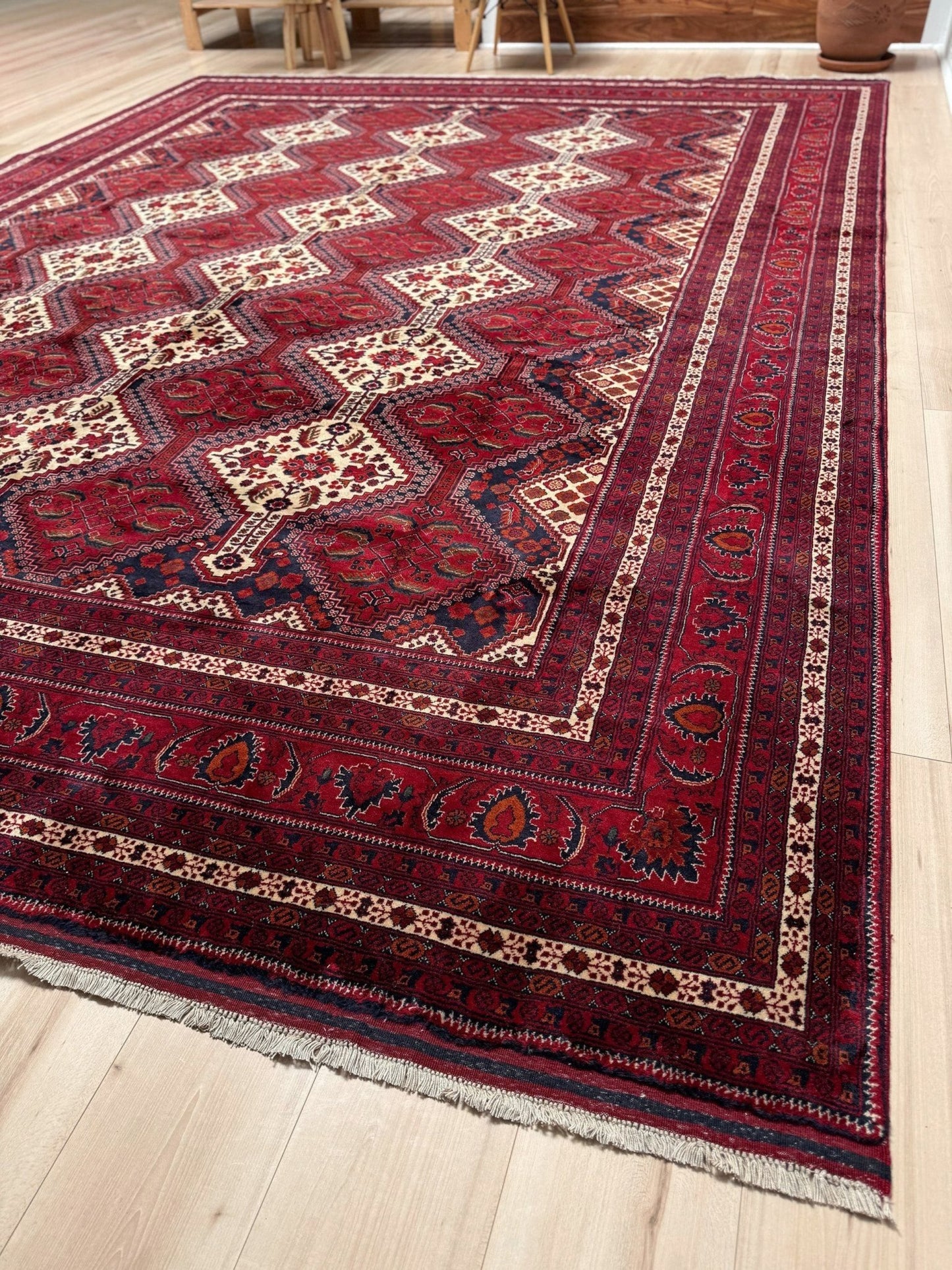 A traditional Persian-style area rug with a deep red field, cream and navy geometric medallions, and ornate borders, shown on a light wood floor.
