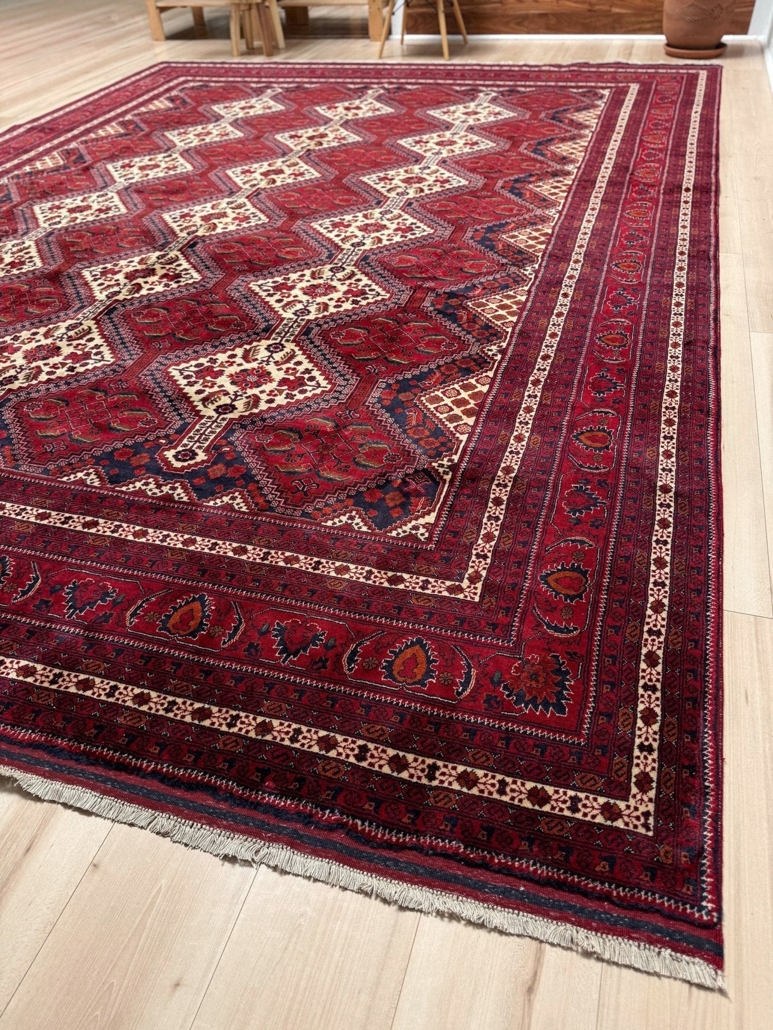 A traditional Persian-style area rug with a deep red field, cream and navy geometric medallions, and ornate borders, shown on a light wood floor.