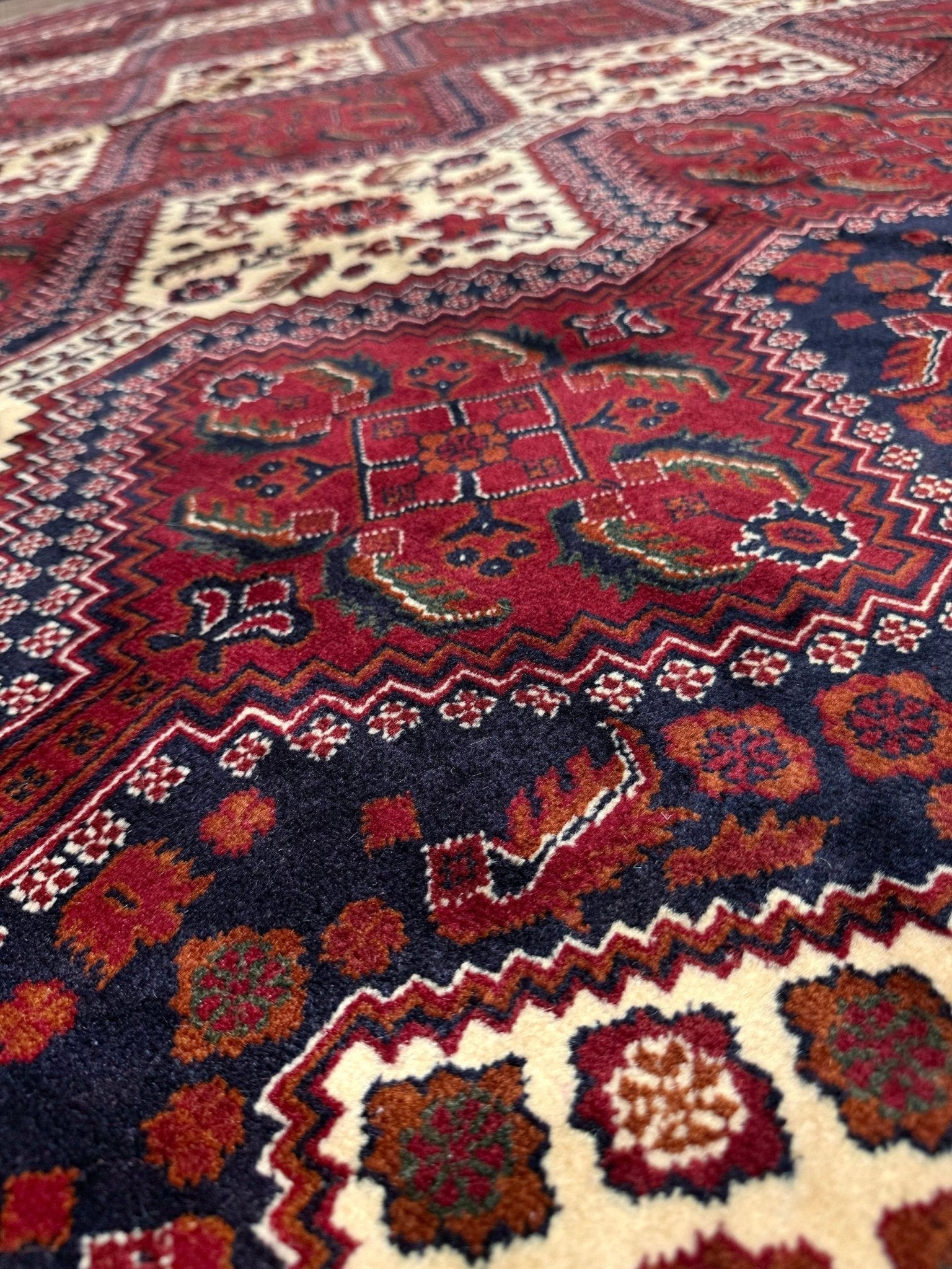 A close-up view of a traditional khal mohammadi patterned rug with a deep red central medallion, dark navy blue sections, and cream borders with floral motifs.