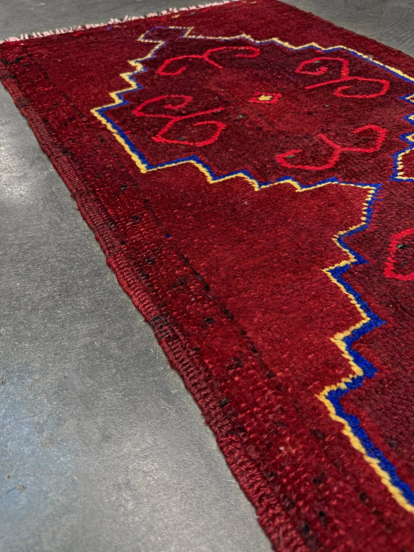 Vintage Turkish Yastik rug in deep cherry red with fuchsia hot pink tribal motifs, blue outlines, and yellow highlights. Hand-knotted wool, 20x43 inches. One-of-a-kind piece from Indigo Rugs, the best rug shop in the San Francisco Bay Area (Burlingame, CA). Free shipping included.