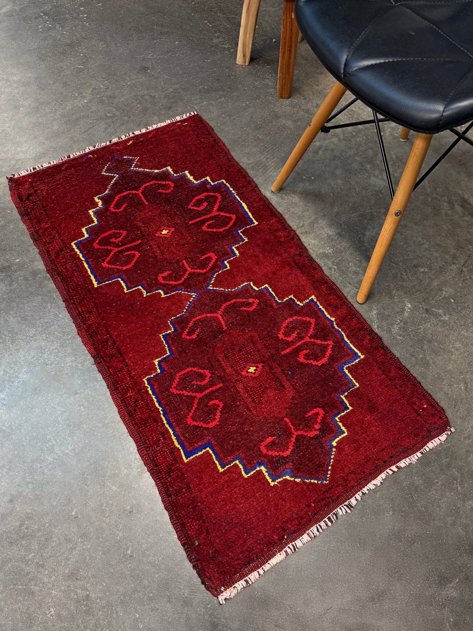 Vintage Turkish Yastik rug in deep cherry red with fuchsia tribal motifs, blue outlines, and yellow highlights. Hand-knotted wool, 20x43 inches. One-of-a-kind piece from Indigo Rugs, the best rug shop in the San Francisco Bay Area (Burlingame, CA). Free shipping included.