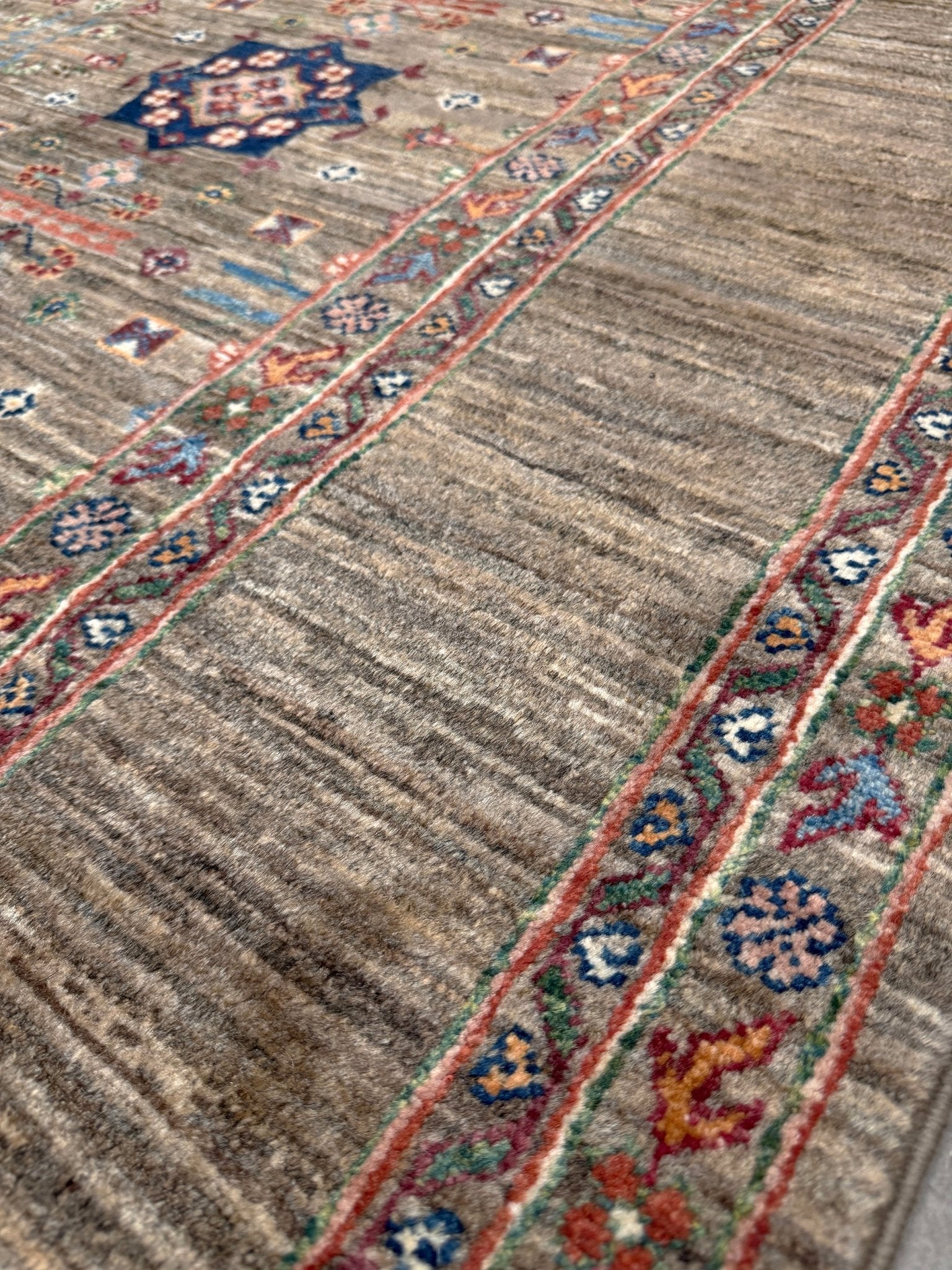 Contemporary Bilcik Turkmen 7x10 rug with dusted olive taupe field, colorful tribal motifs, decorative tassels, handmade Ghazni wool area rug from Indigo Rugs Burlingame Bay Area.