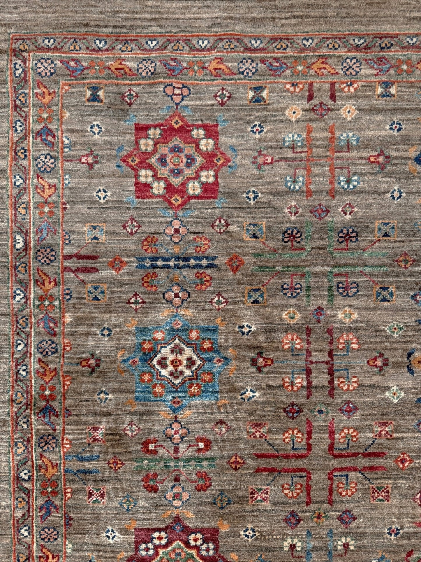 Contemporary Bilcik Turkmen 7x10 rug with dusted olive taupe field, colorful tribal motifs, decorative tassels, handmade Ghazni wool area rug from Indigo Rugs Burlingame Bay Area.