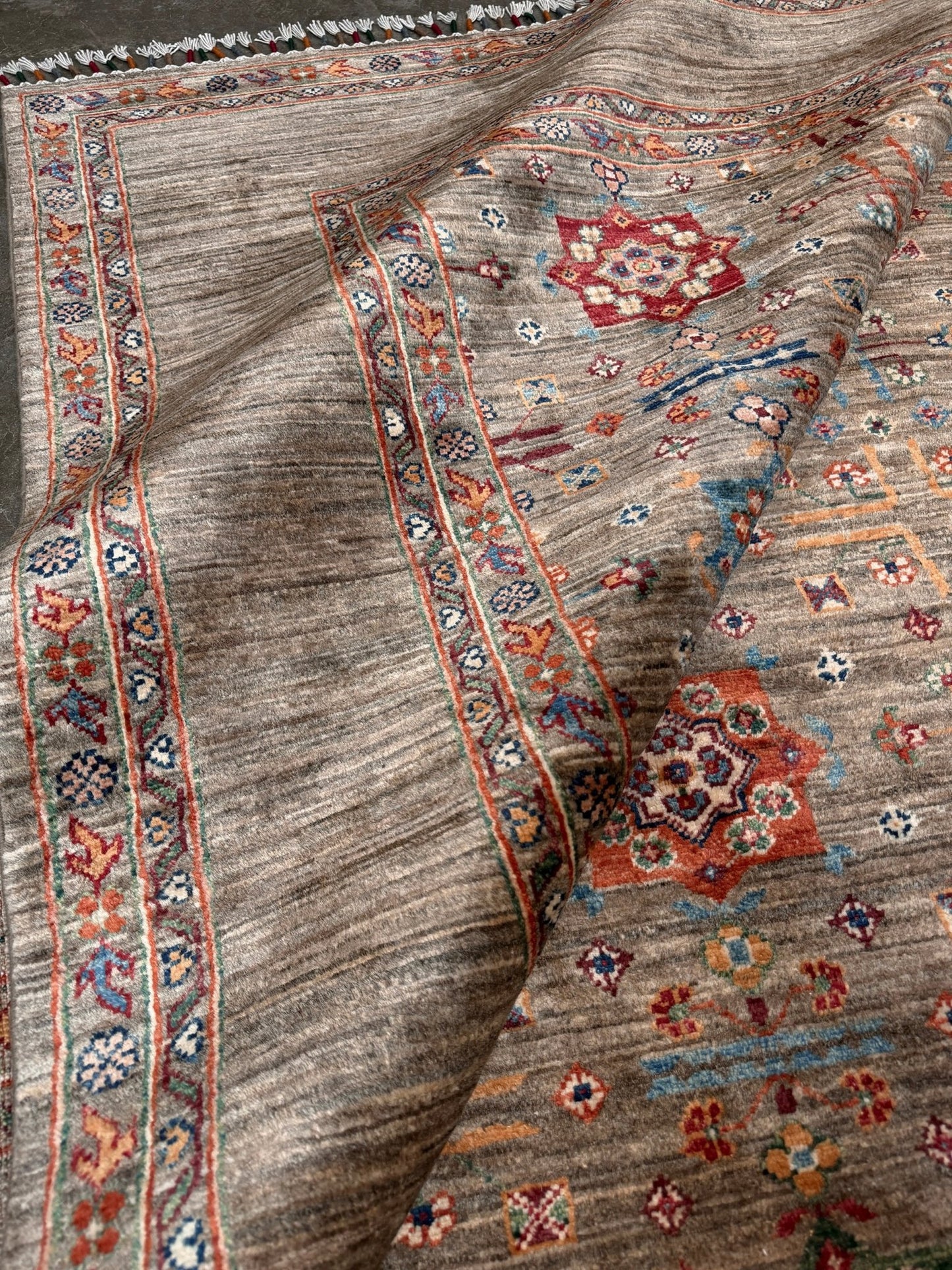 Contemporary Bilcik Turkmen 7x10 rug with dusted olive taupe field, colorful tribal motifs, decorative tassels, handmade Ghazni wool area rug from Indigo Rugs Burlingame Bay Area.
