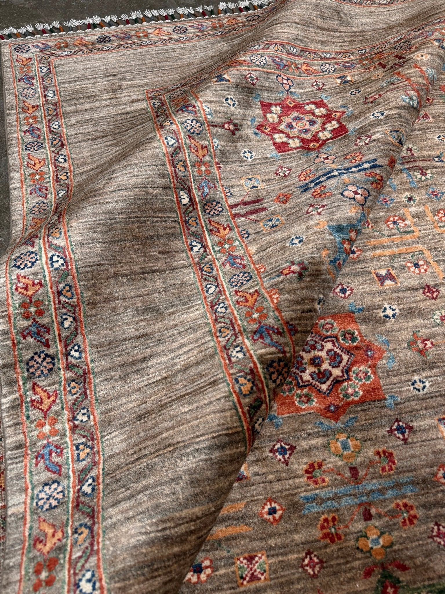 Contemporary Bilcik Turkmen 7x10 rug with dusted olive taupe field, colorful tribal motifs, decorative tassels, handmade Ghazni wool area rug from Indigo Rugs Burlingame Bay Area.