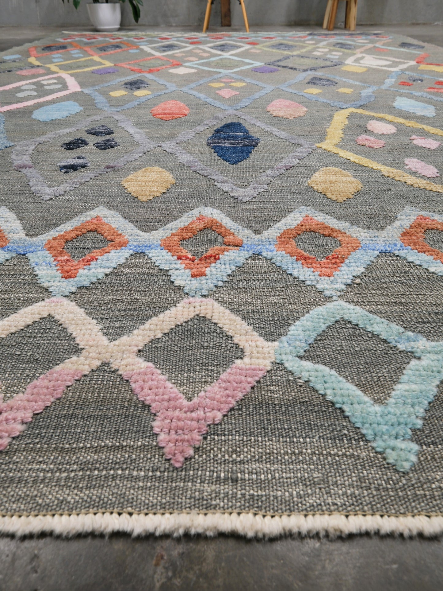 Multicolored geometric patterned rug on a dark floor. Warm gray vibrant modern Turkish Tulu rug with colorful raised diamond motifs, 3D wool pile texture, handmade wool area rug 9x12 from Indigo Rugs Burlingame Bay Area.