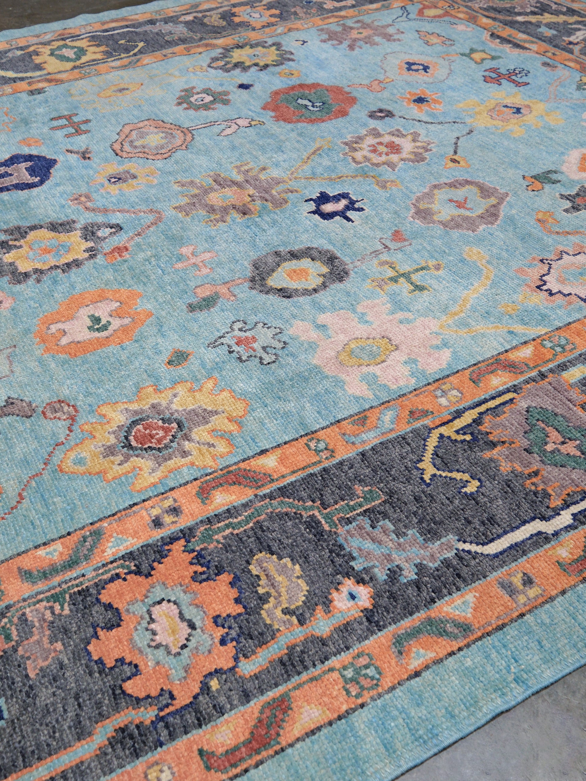 Pale turquoise Turkish Oushak rug with charcoal border, coral orange framing, and colorful abstract floral motifs, hand-knotted wool 8x10 area rug from Indigo Rugs Burlingame Bay Area.