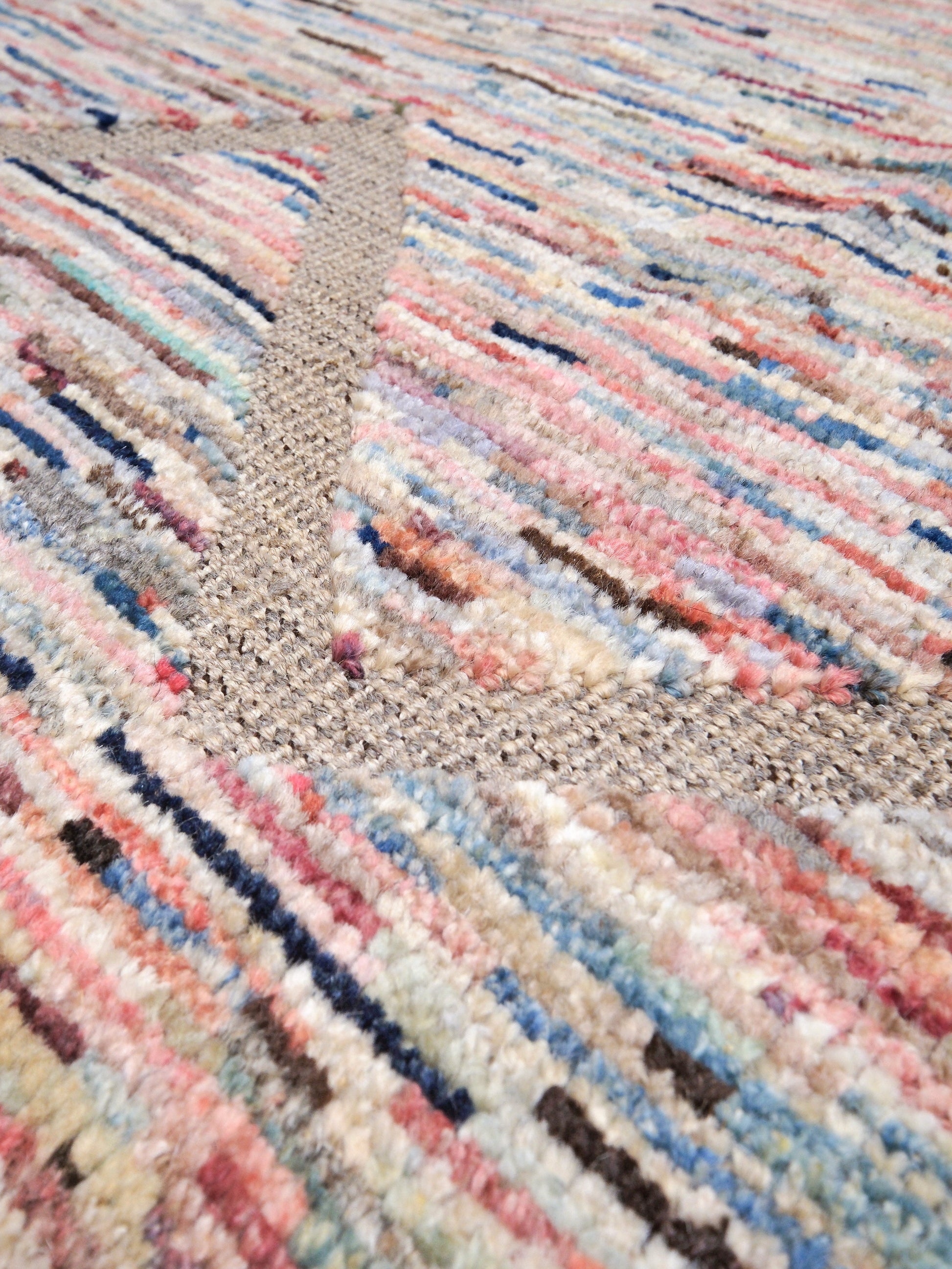 Close-up of a textured woven rug with a multicolor striped pattern in pink, blue, beige, and cream.