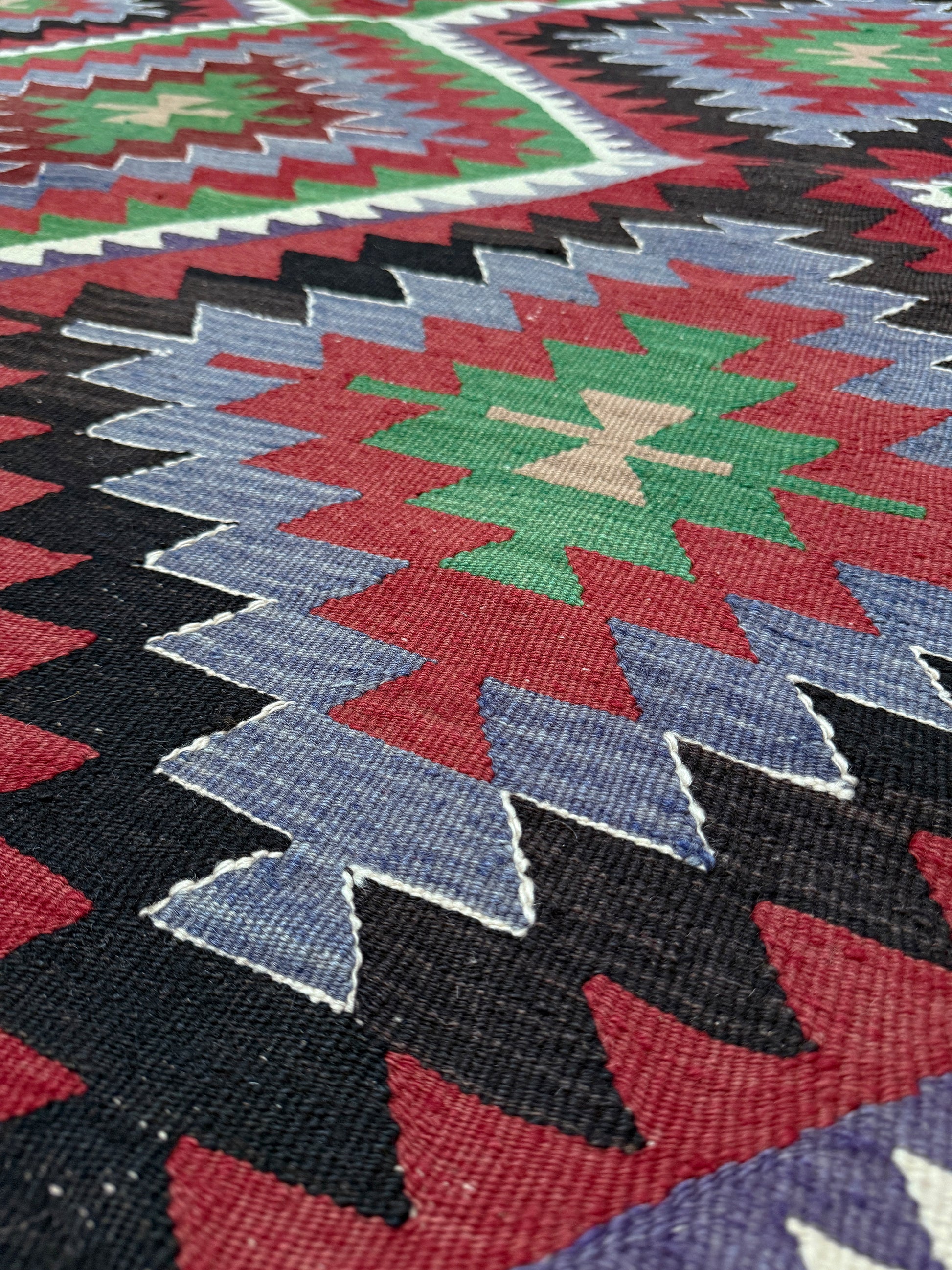 Close-up of a colorful geometric patterned rug with red, blue, green, and black colors. Vintage Esme Turkish kilim featuring navajo style geometric design, handwoven wool flatweave rug 6x9