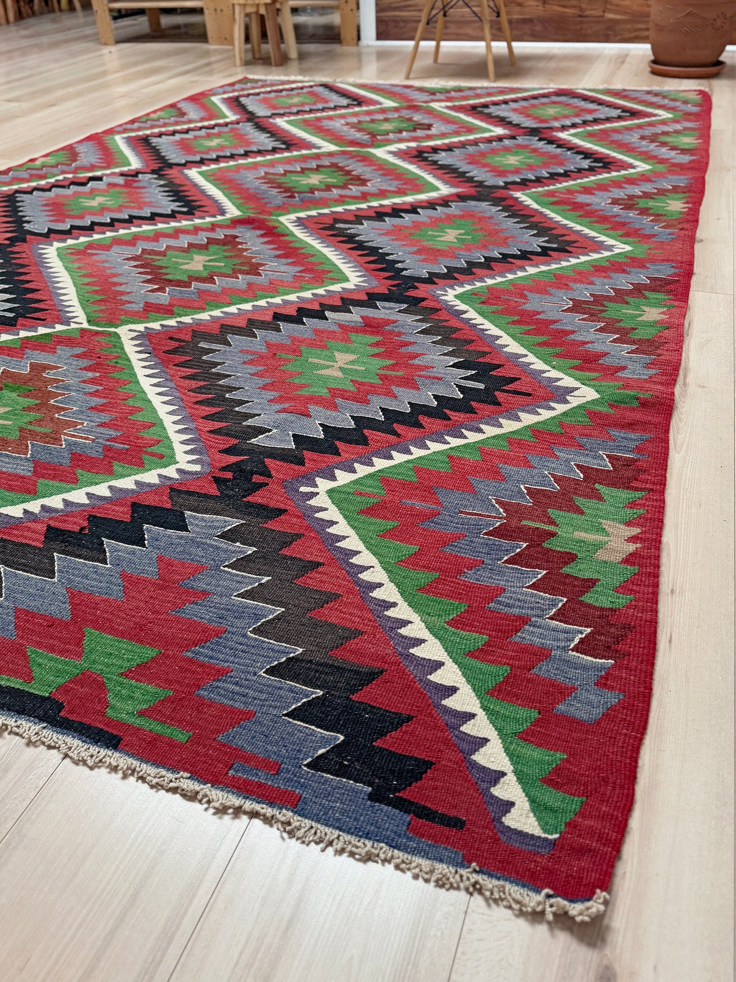 Colorful geometric patterned rug on a wooden floor. Vintage Esme Turkish kilim featuring navajo style geometric design, handwoven wool flatweave rug 6x9