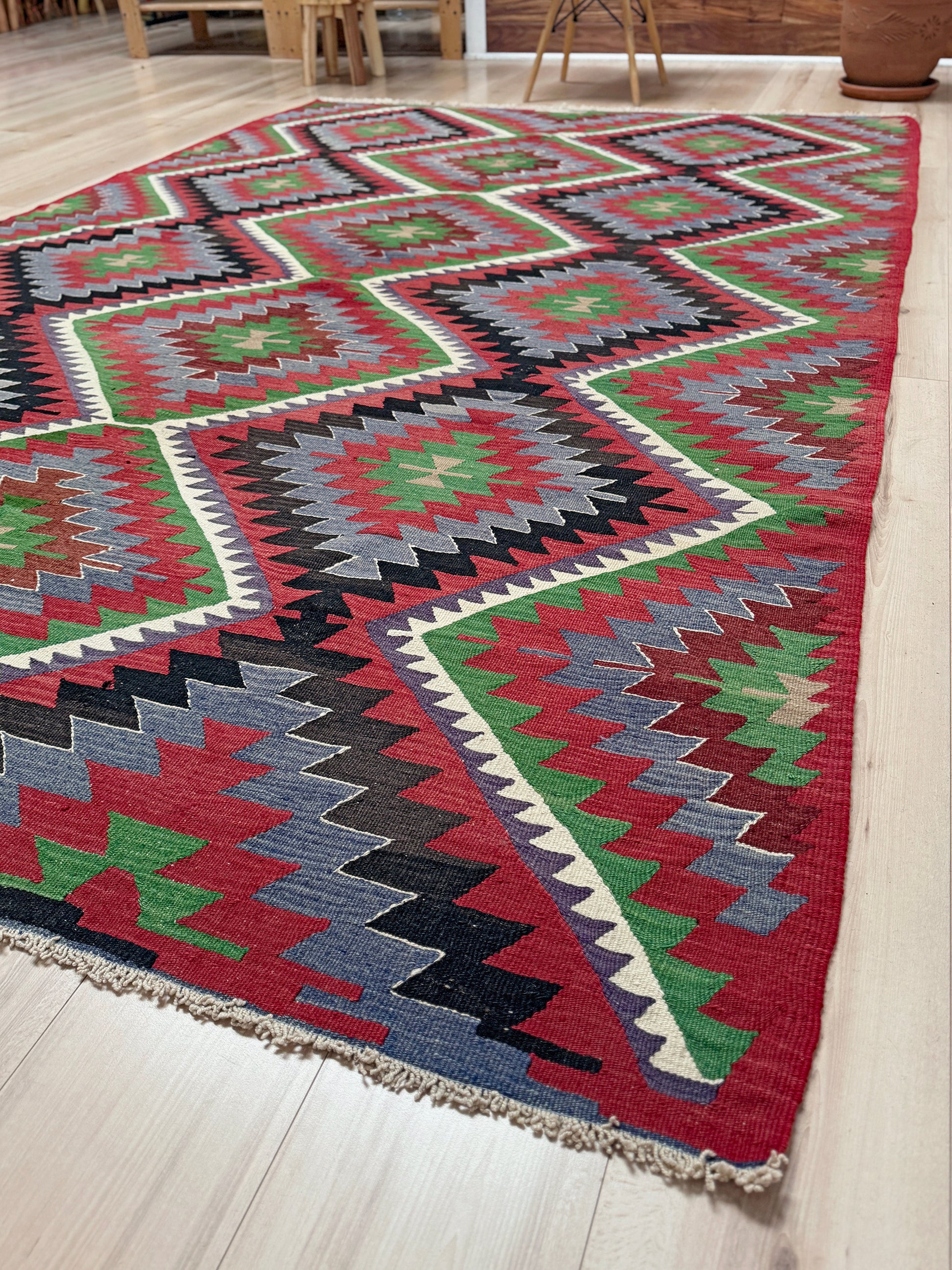 Colorful geometric patterned rug on a wooden floor. Vintage Esme Turkish kilim featuring navajo style geometric design, handwoven wool flatweave rug 6x9