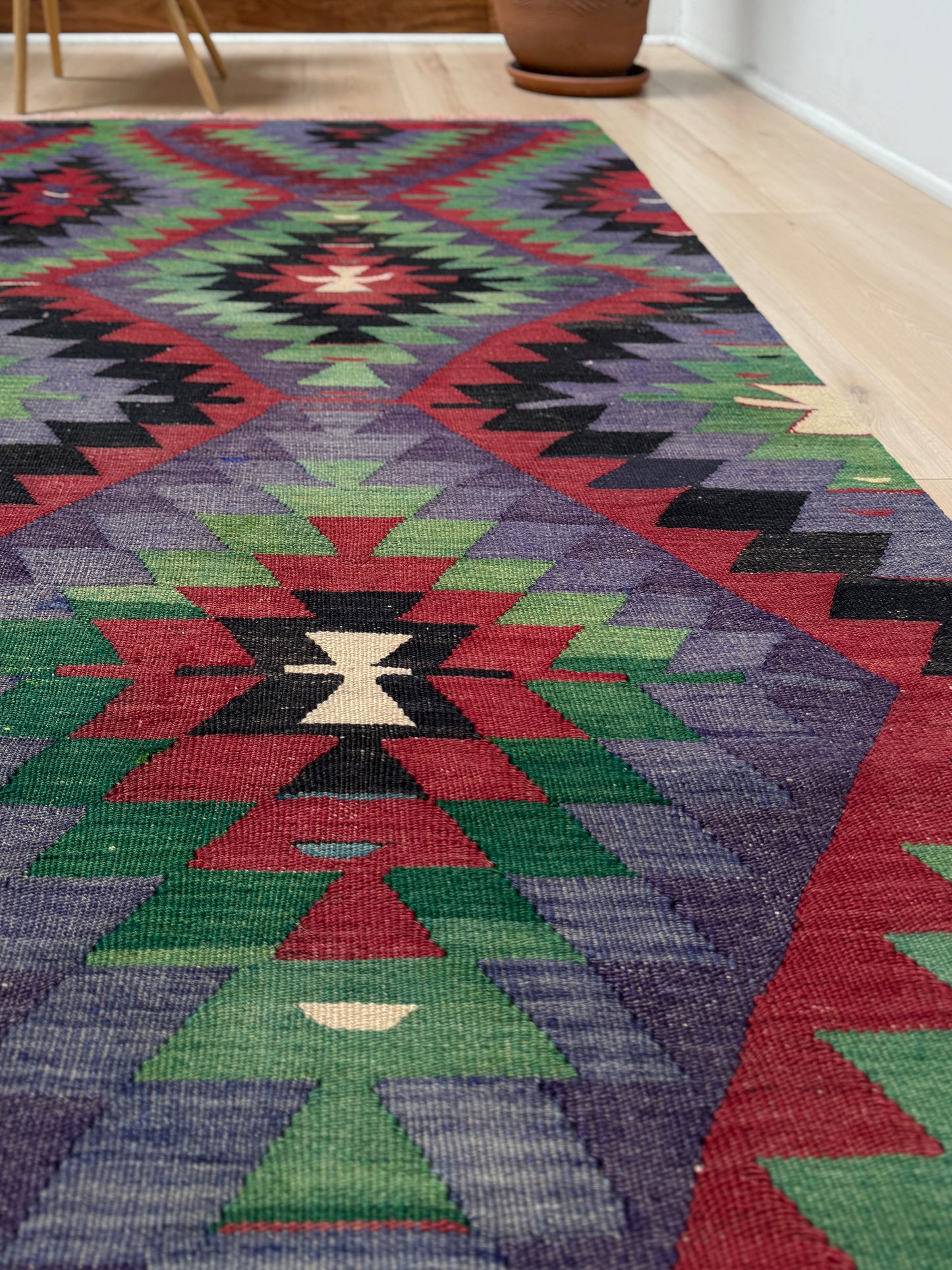 Colorful geometric patterned rug on a wooden floor. Vintage Esme Turkish tribal kilim rug featuring geometric design in raspberry red, blue violet, emerald green, handmade 6x10 perfect for boho style 