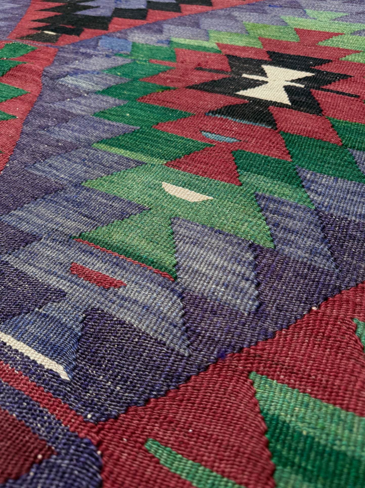 Close-up of a colorful patterned fabric with geometric design. Vintage Esme Turkish tribal kilim rug featuring geometric design in raspberry red, blue violet, emerald green, handmade 6x10 perfect for boho style 