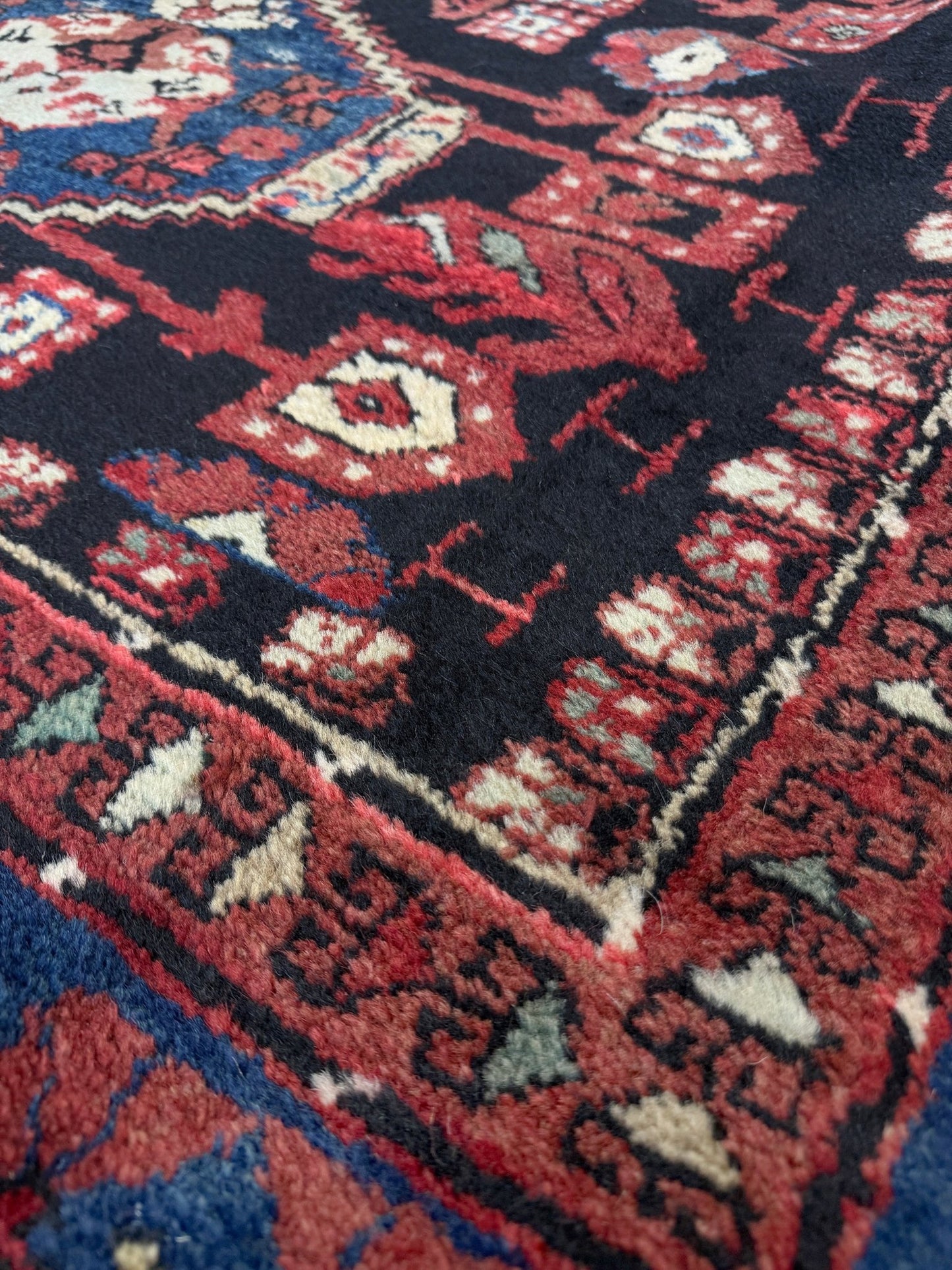 Close-up of a patterned rug with red, blue, and white colors. vintage Komurcu Kula Turkish rug with black brown field, madder red borders, handmade wool area rug 6x10 from Indigo Rugs Burlingame Bay Area.