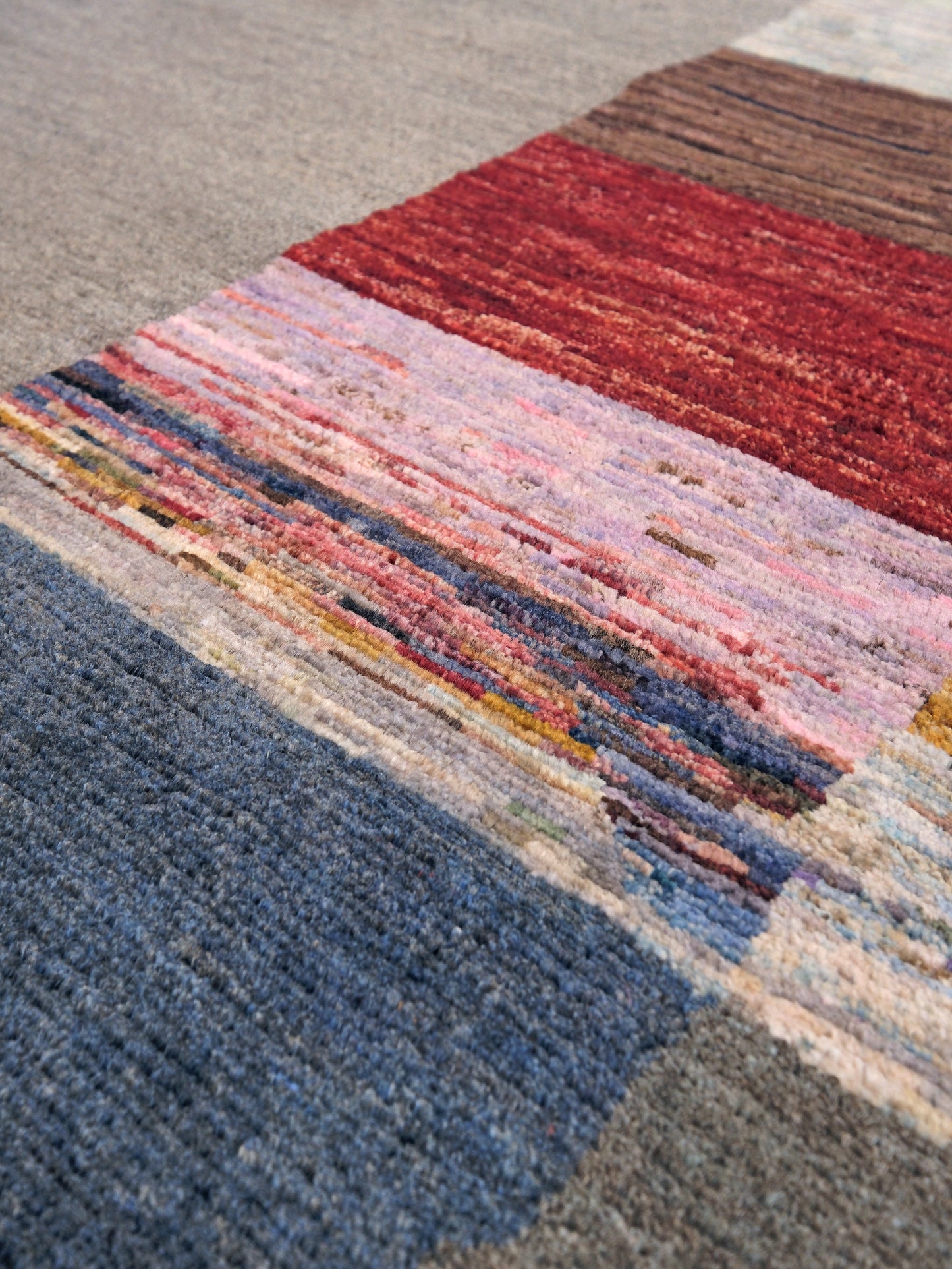 A close-up of a textured area rug with a geometric, striped pattern in shades of red, pink, blue, gray, and beige.
