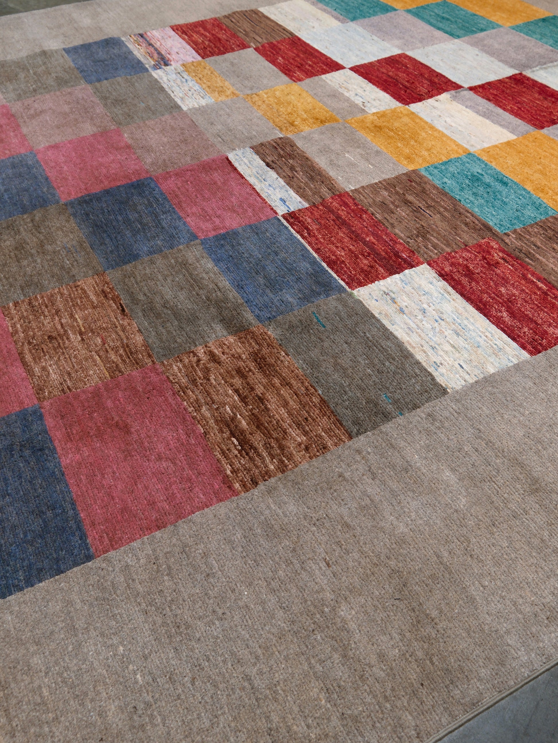 A close-up of a textured area rug featuring a multicolor patchwork design with a solid taupe border.