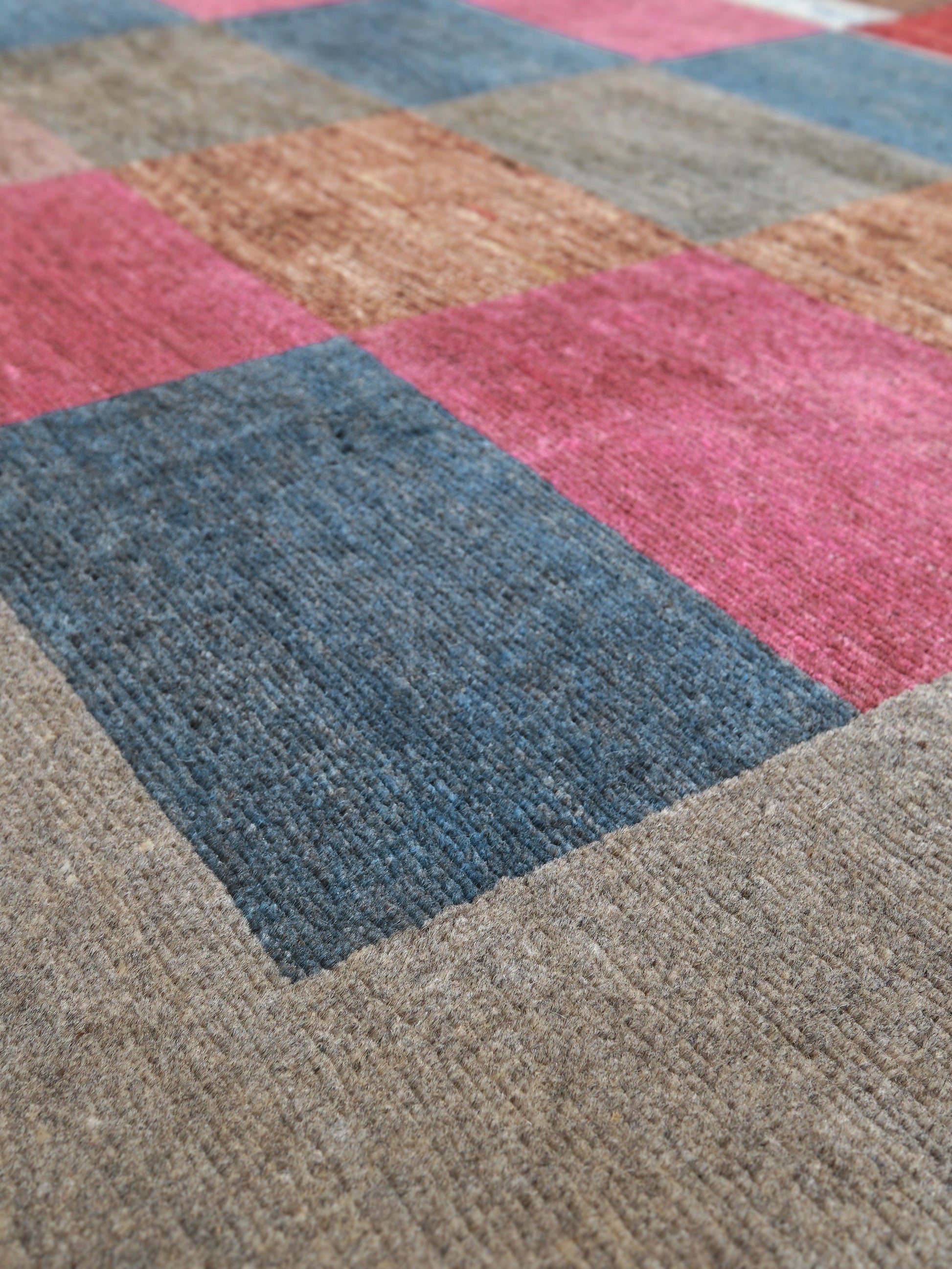 Close-up of a textured patchwork rug with large geometric blocks in dusty blue, pink, tan, and taupe.