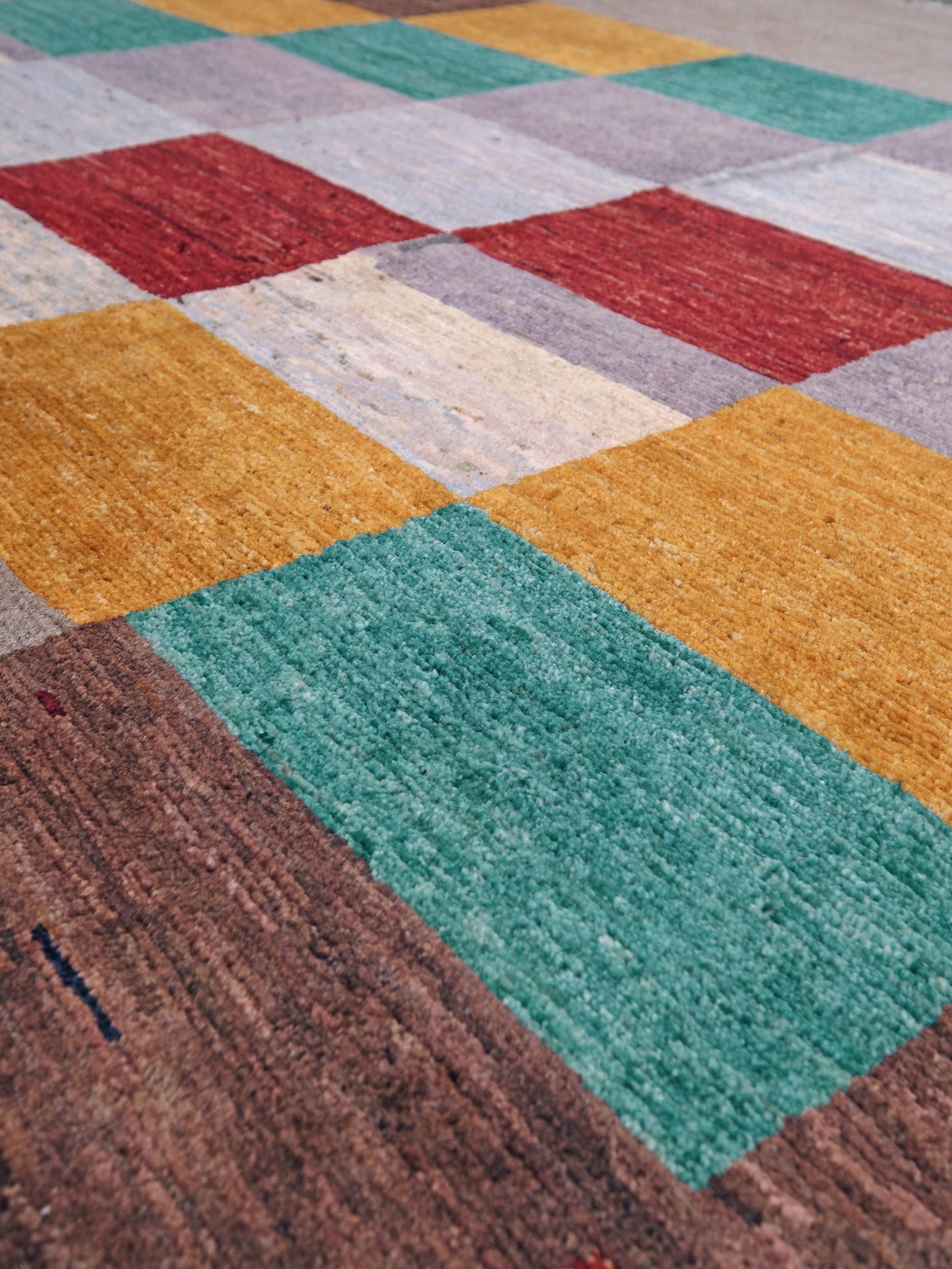 A close-up of a multicolor patchwork area rug with textured rectangular blocks in teal, mustard yellow, red, brown, beige, and light gray.